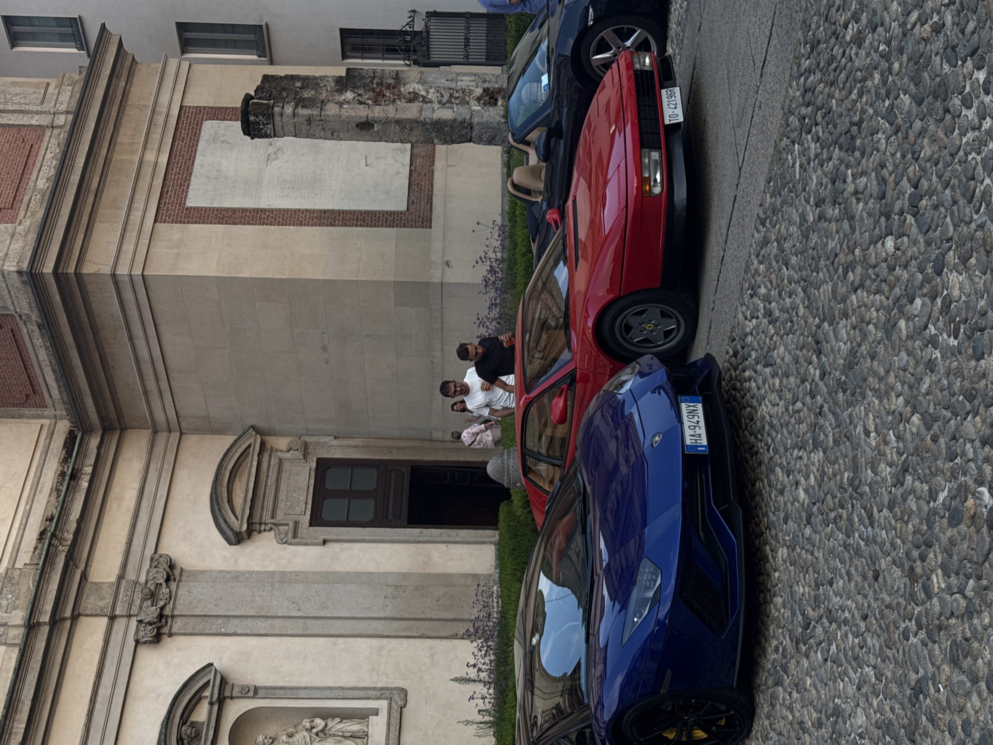 Luxury cars gather on cobblestones outside a Milan church