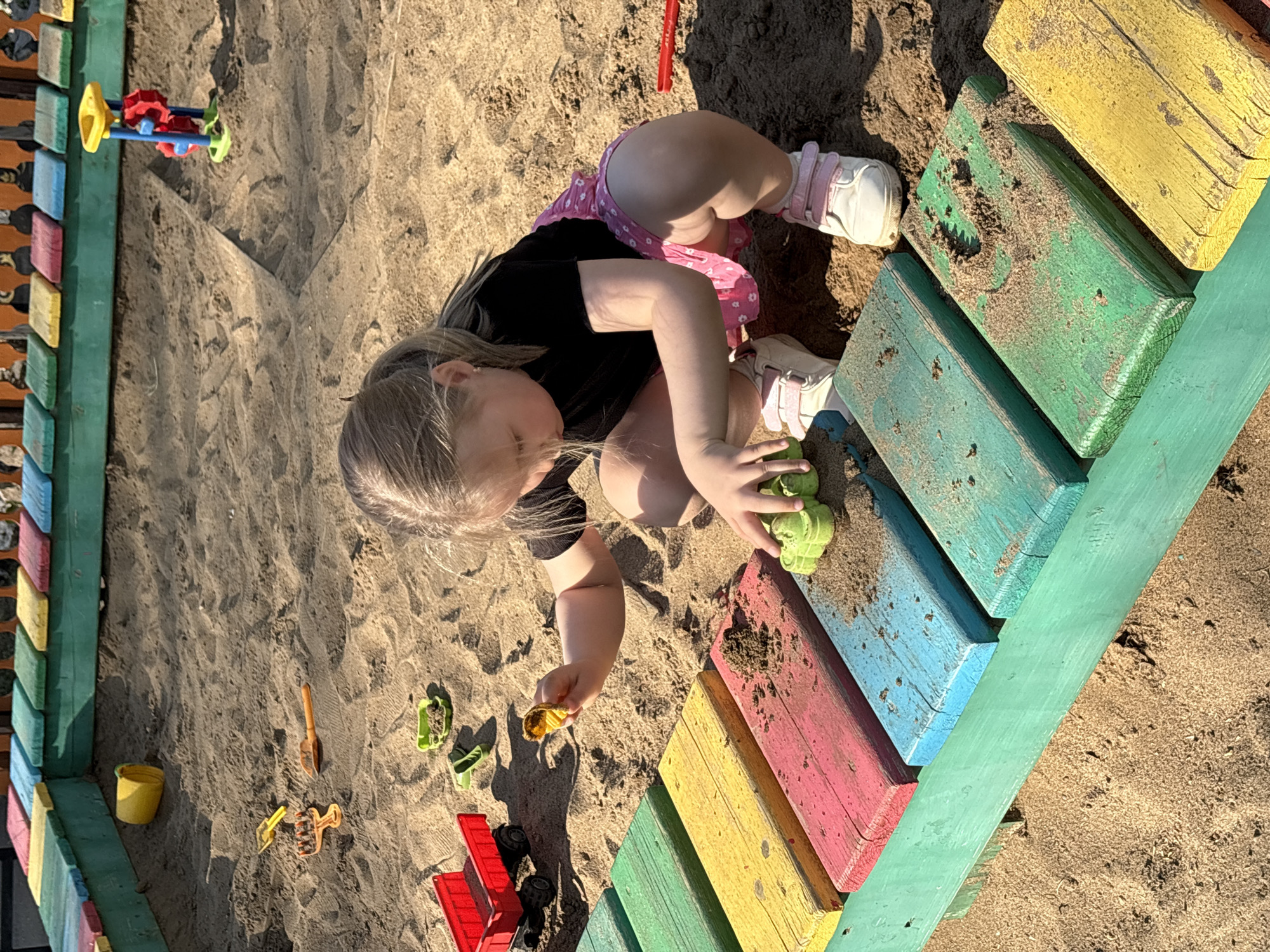 Child plays in sandbox with toys