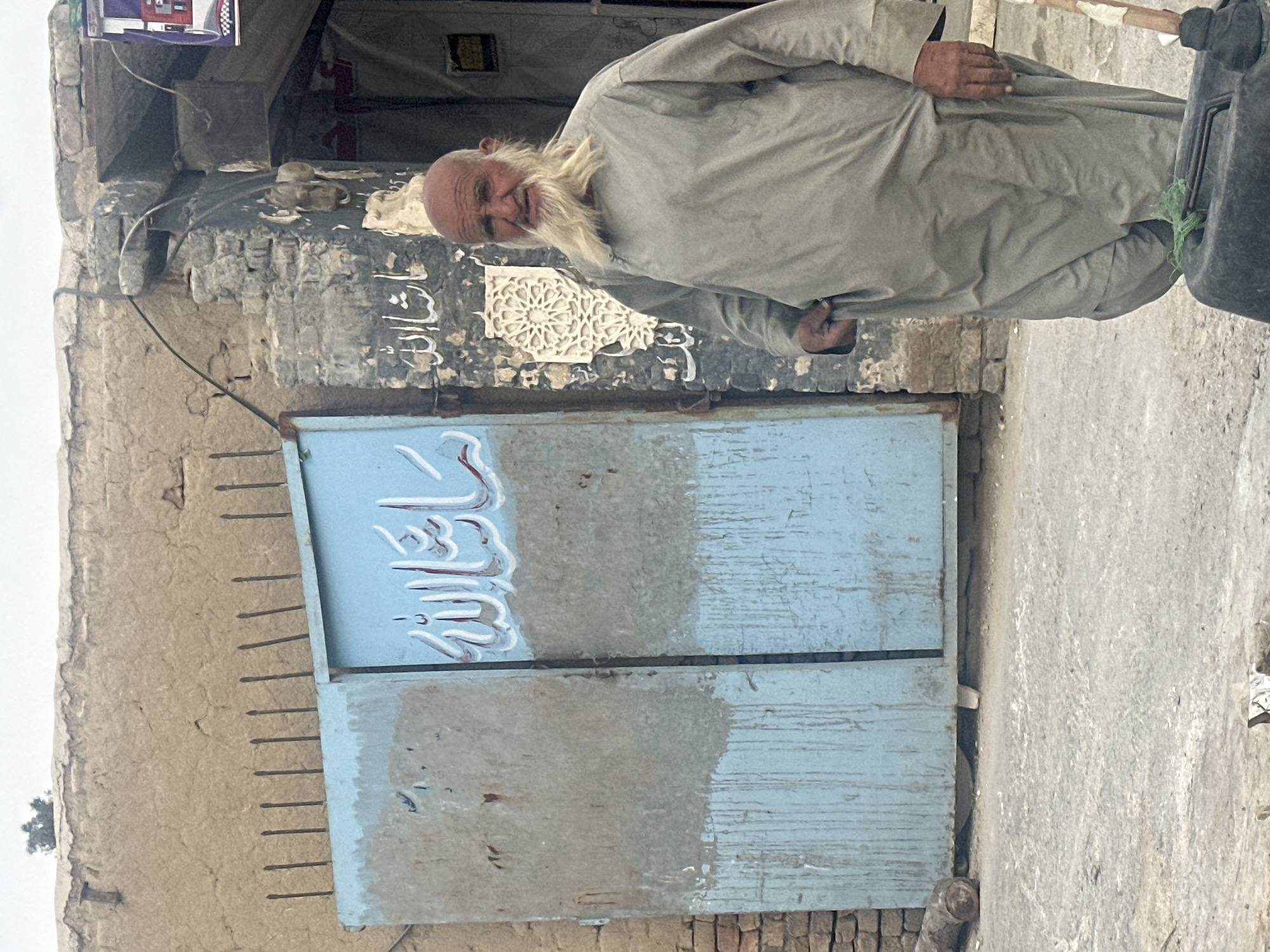 Elderly man stands by weathered blue door in Quetta