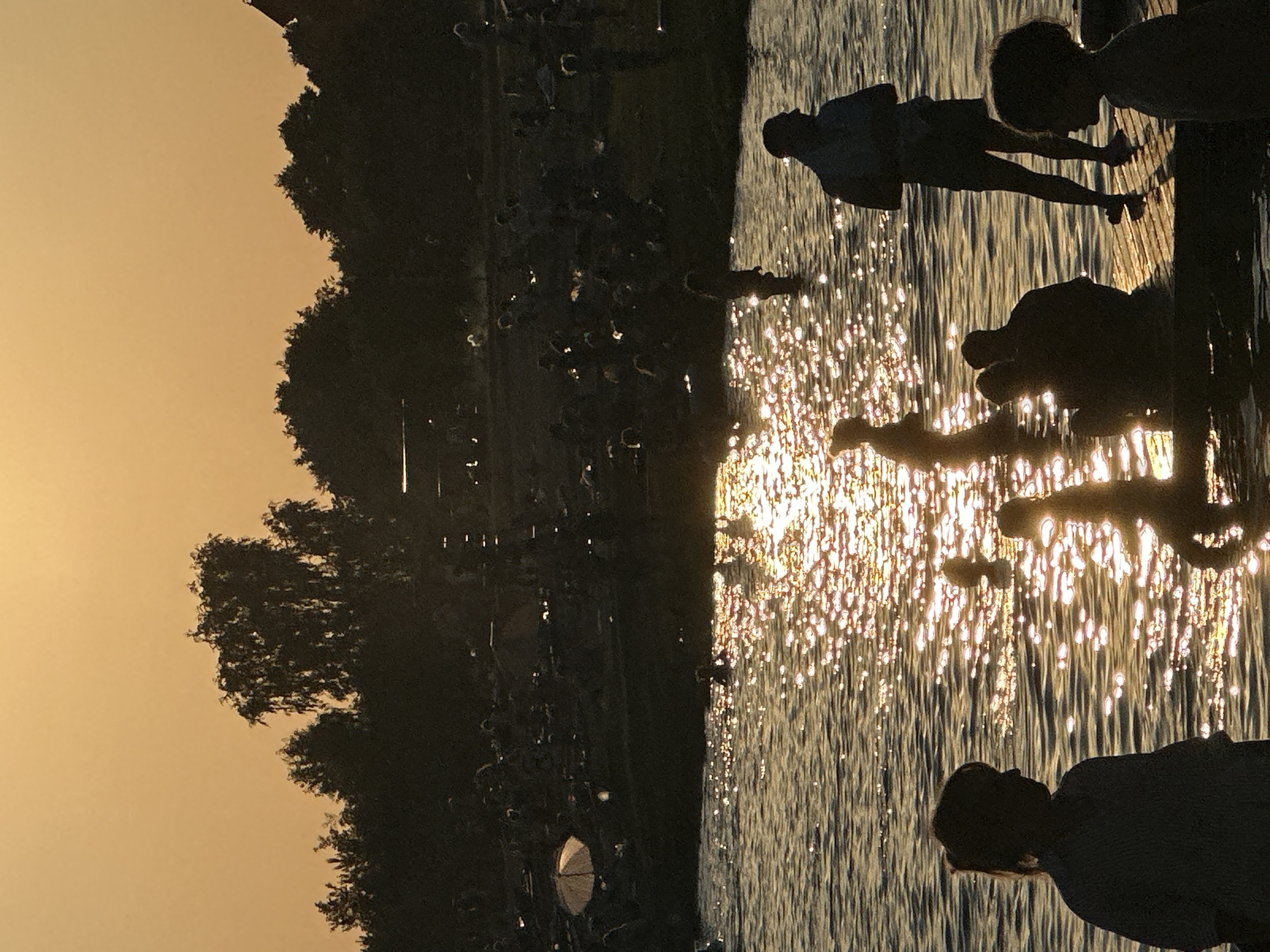 Crowded lakeside beach scene at sunset, swimming and wading