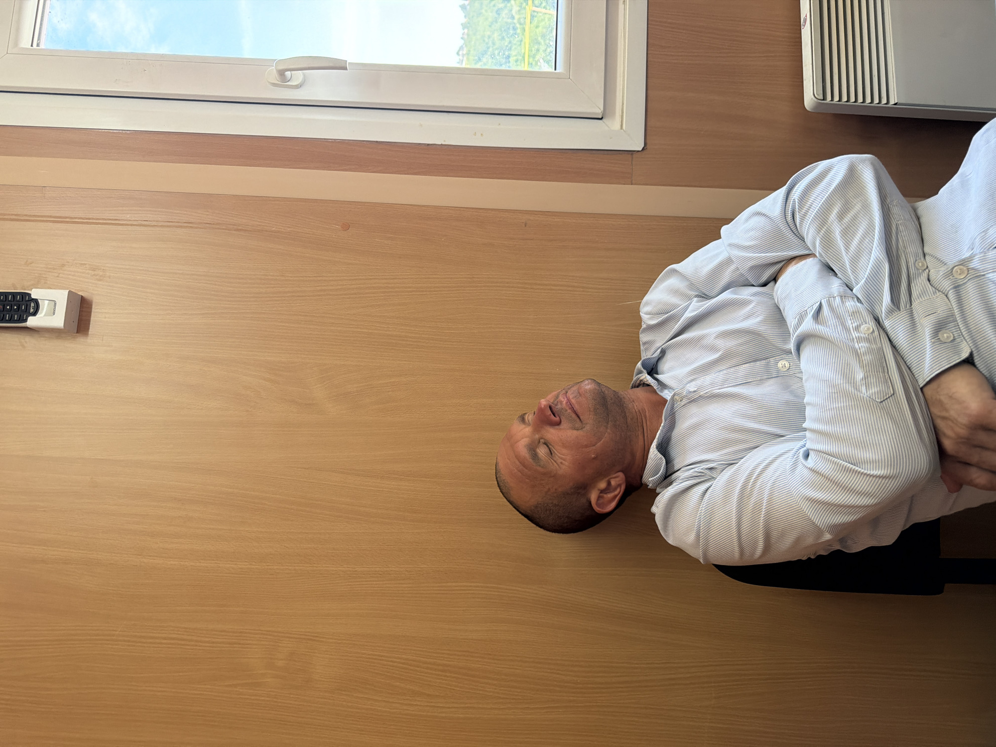 Person asleep in a wood-paneled room, others nearby