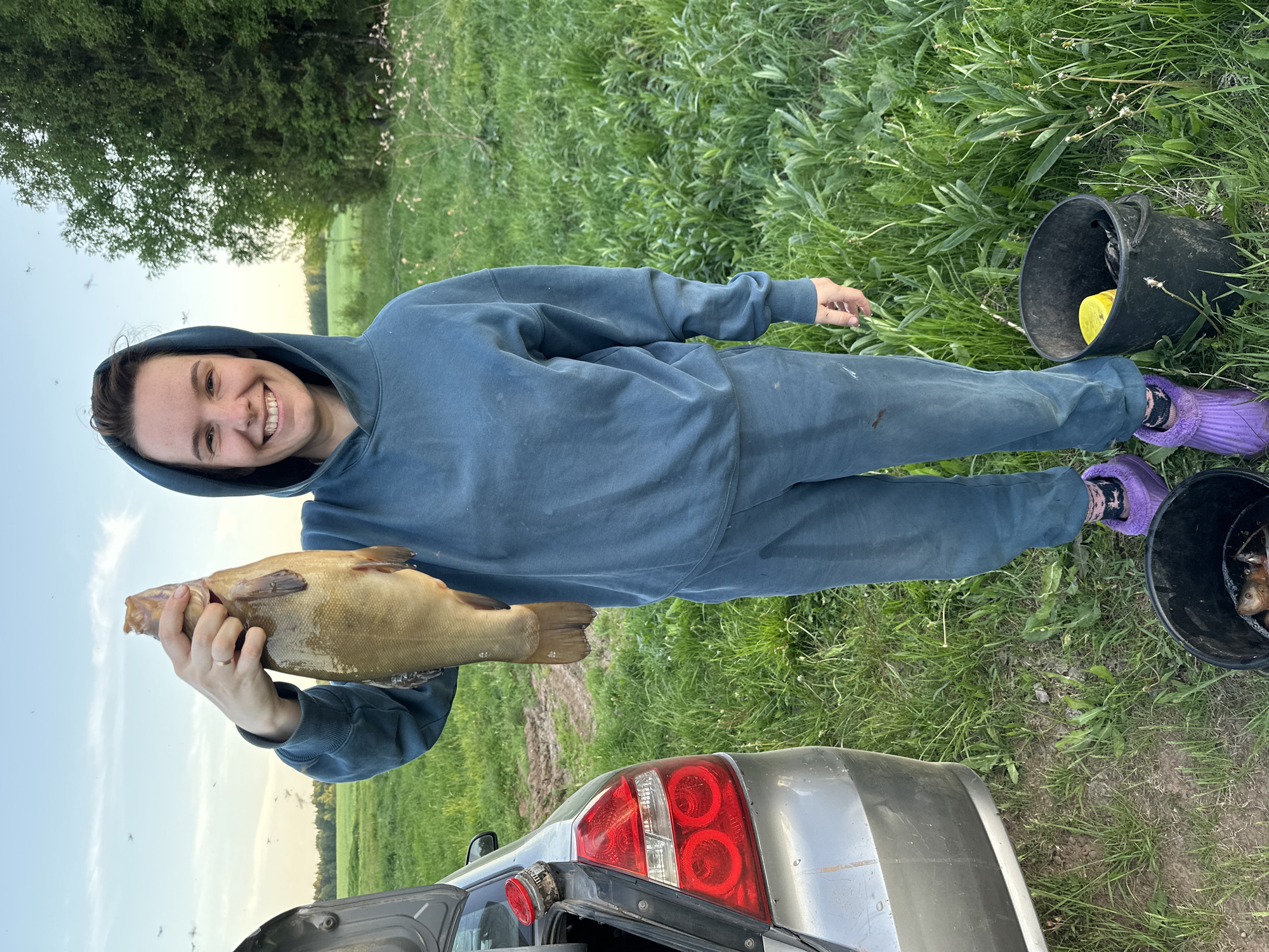 Woman displays large tench fish beside car in Russian field