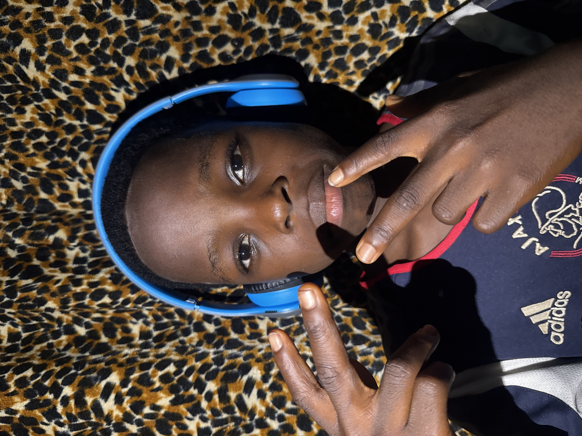 Person relaxes with headphones on leopard-print fabric in Onitsha