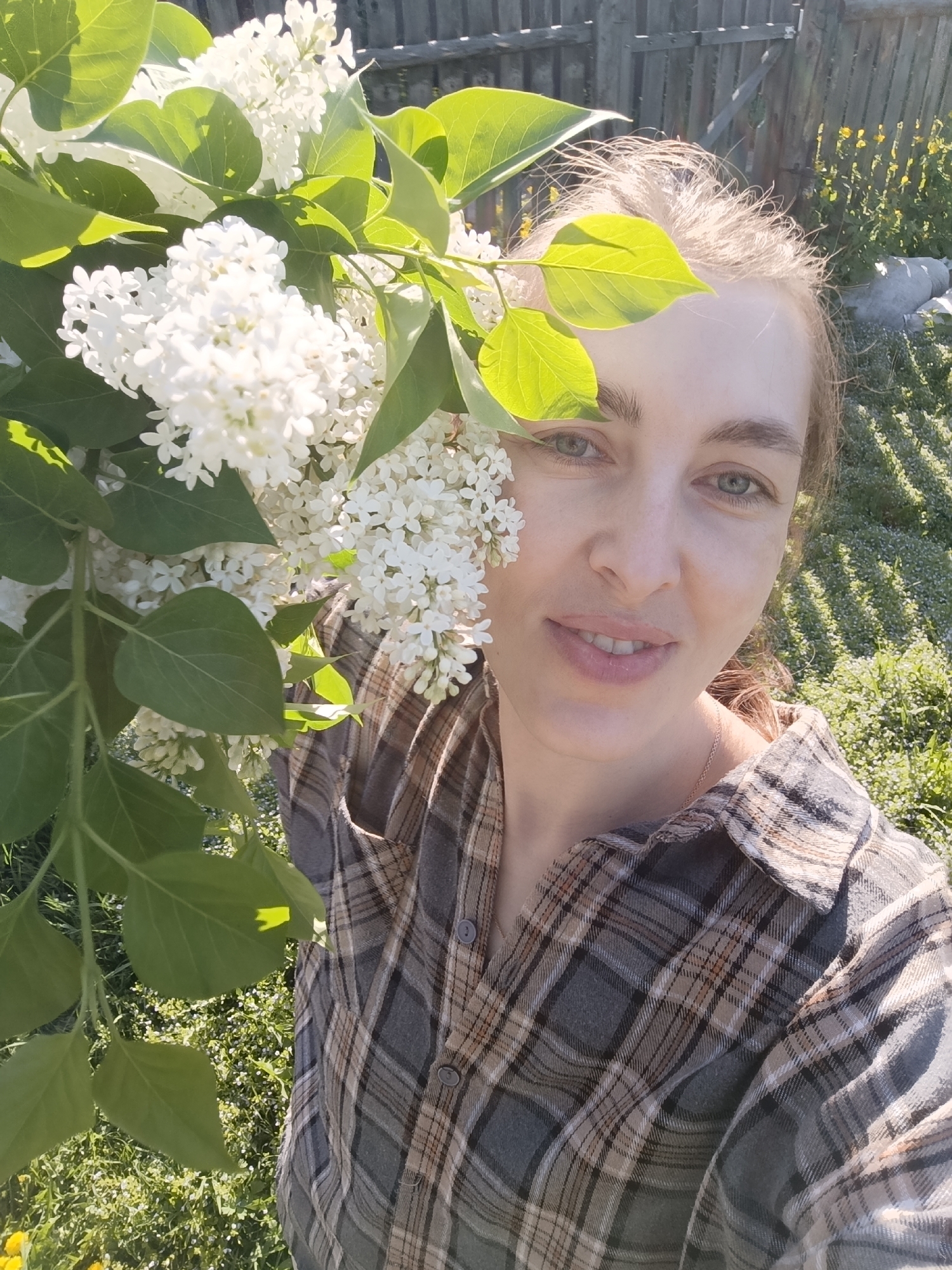 Woman poses near white lilac blossoms in outdoor setting