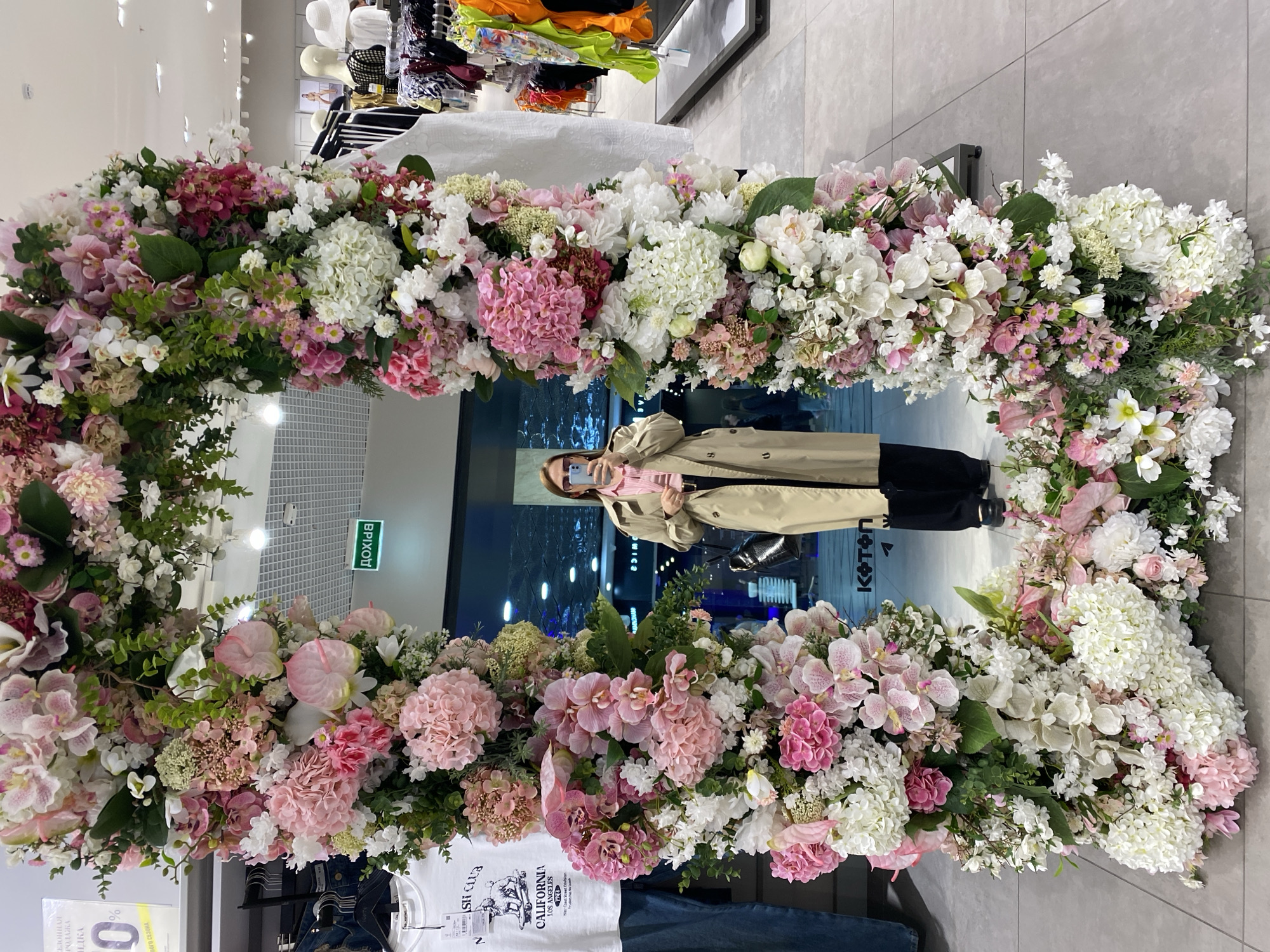 Person in trench coat reflected in flower-adorned mirror, Yekaterinburg