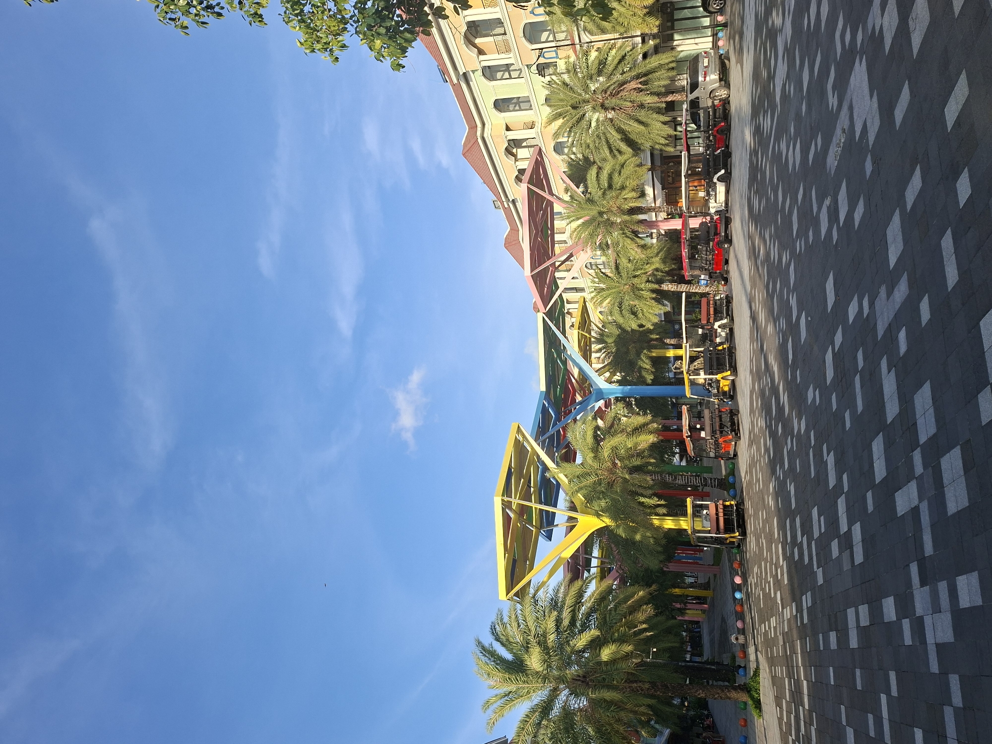 Colorful urban plaza with palms, sculptures, and decorative structures