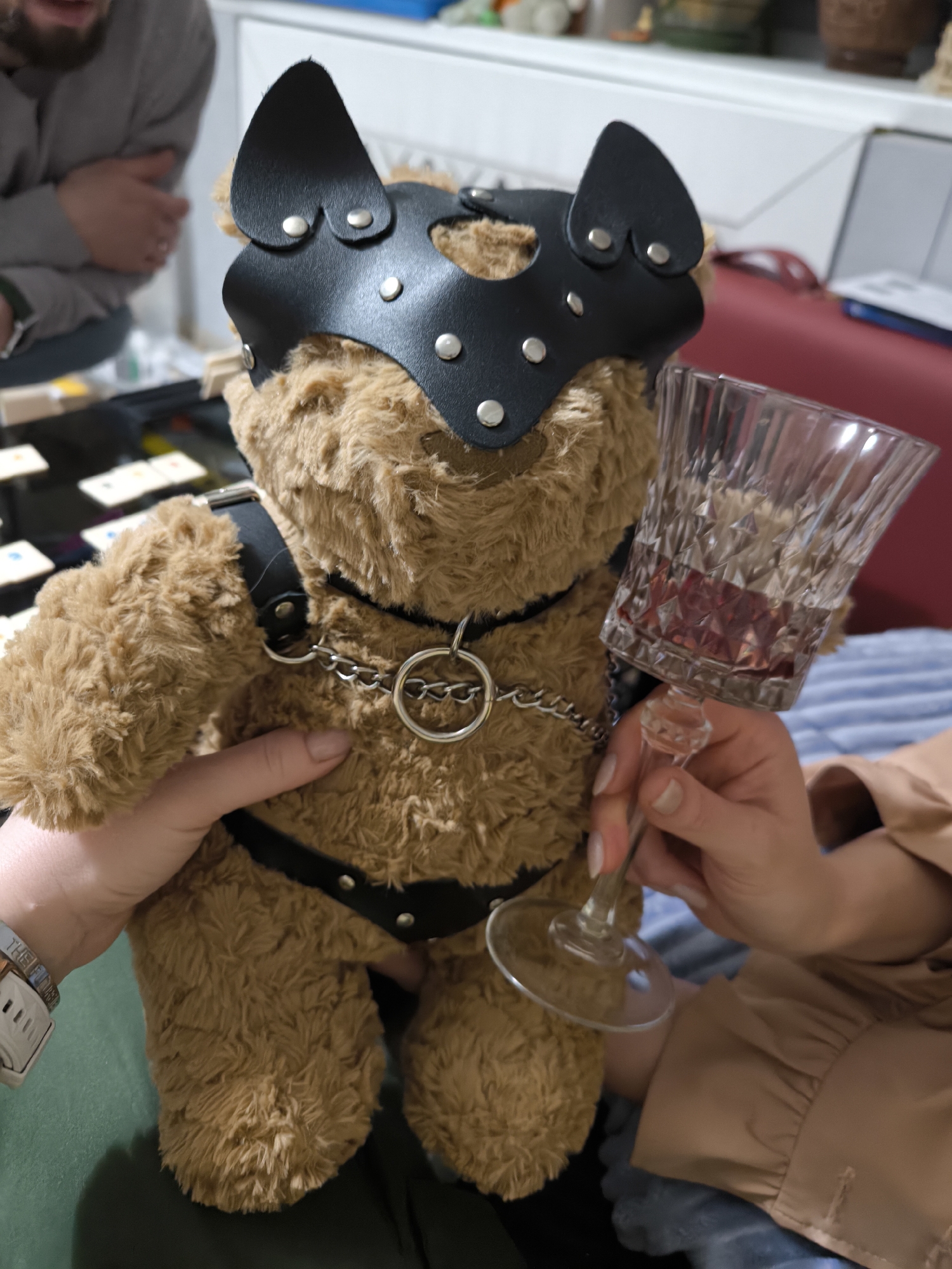 Two people hold leather-clad teddy bear in unknown location