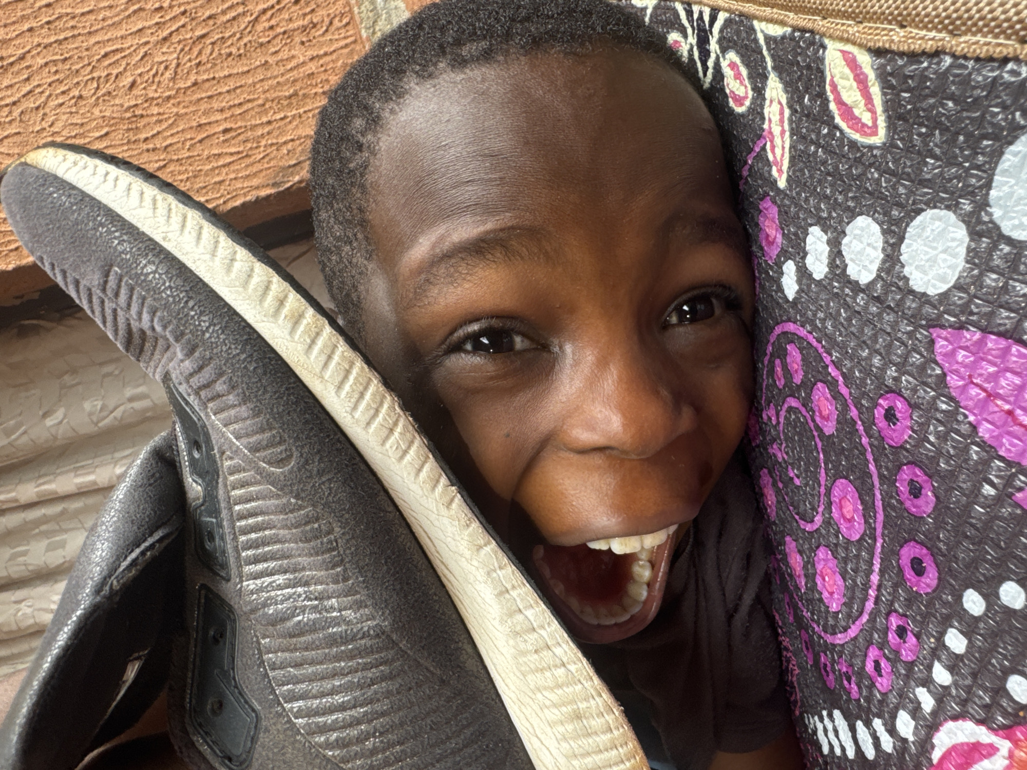 Child on patterned mat, sneaker near face, Onitsha