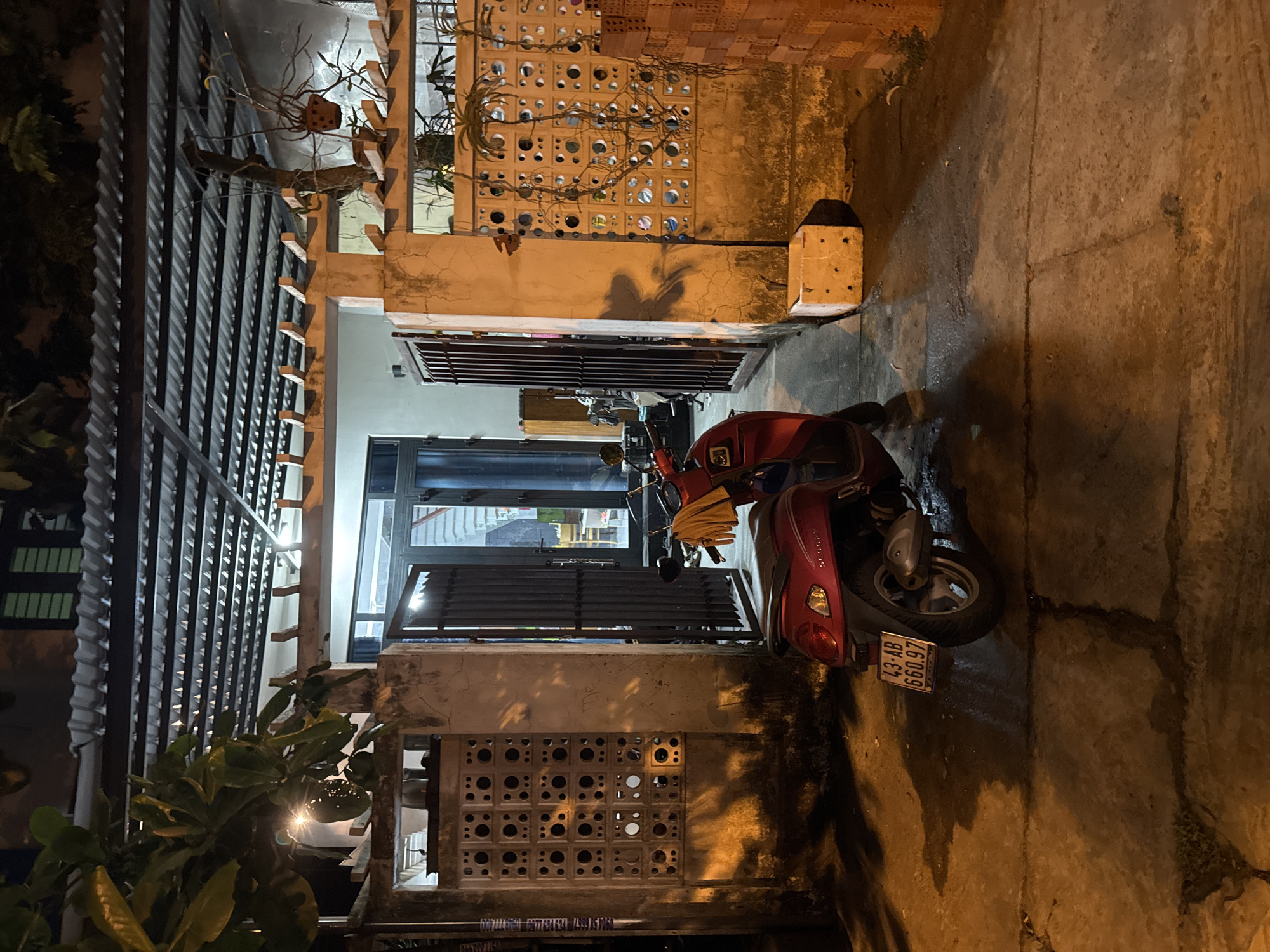 Red scooter parked in worn Đà Nẵng alleyway at night