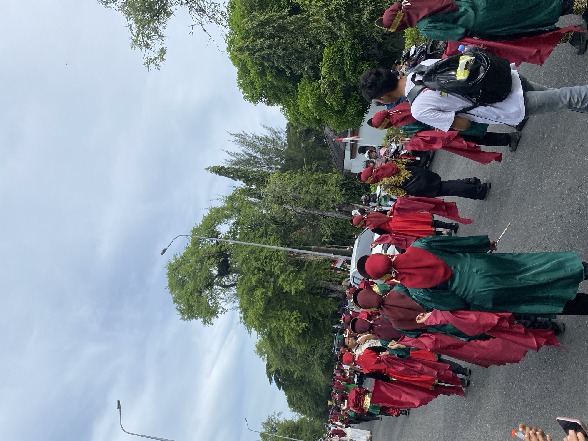 Marching band in red and green parades down a tree-lined street