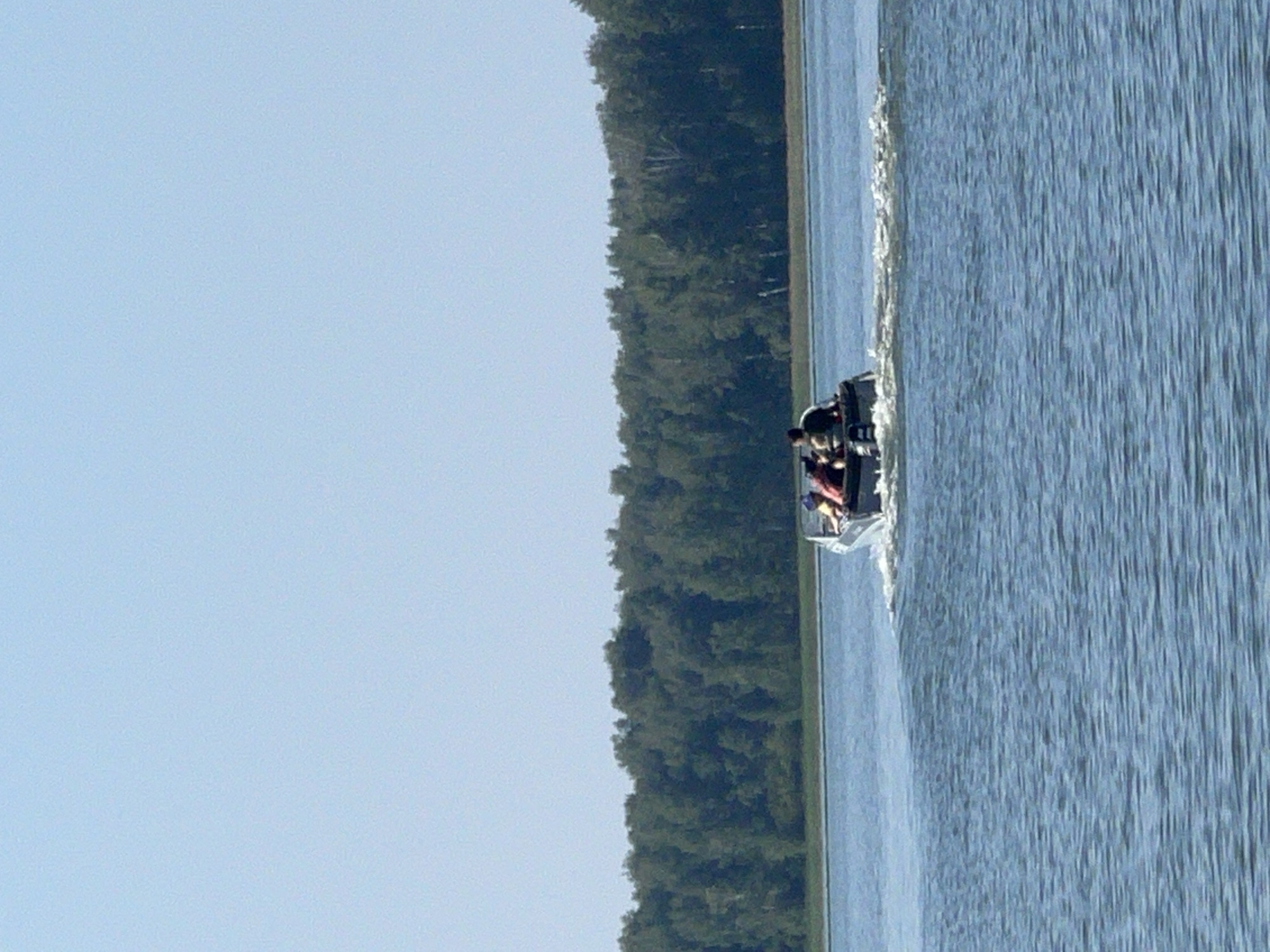 Motorboat crossing calm Russian lake near wooded shoreline