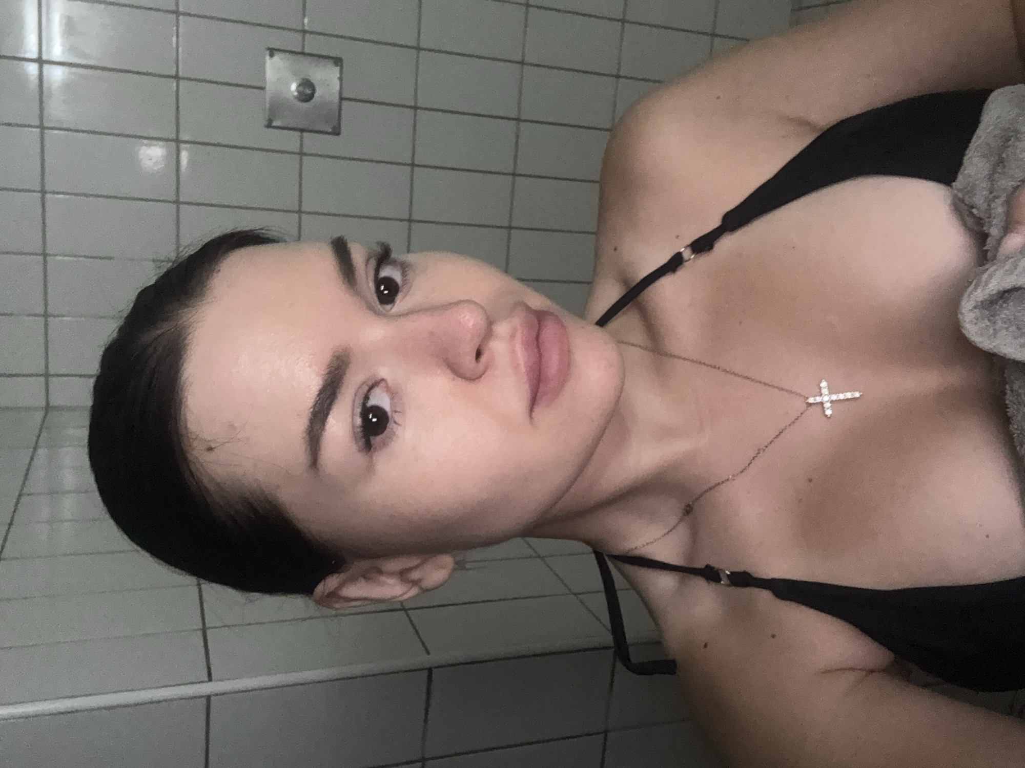 Indoor close-up in a Prague bathroom, black bikini and cross necklace.
