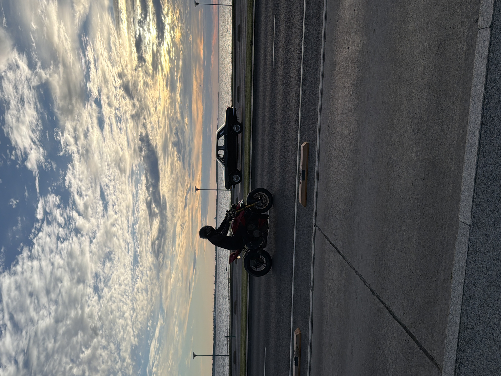 Motorcycle and vintage car silhouetted on Tallinn's coastal road at sunset
