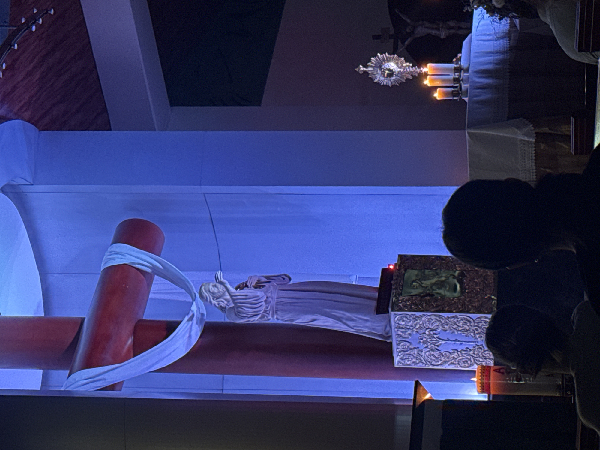 Nighttime religious scene with red crucifix and white statue documented