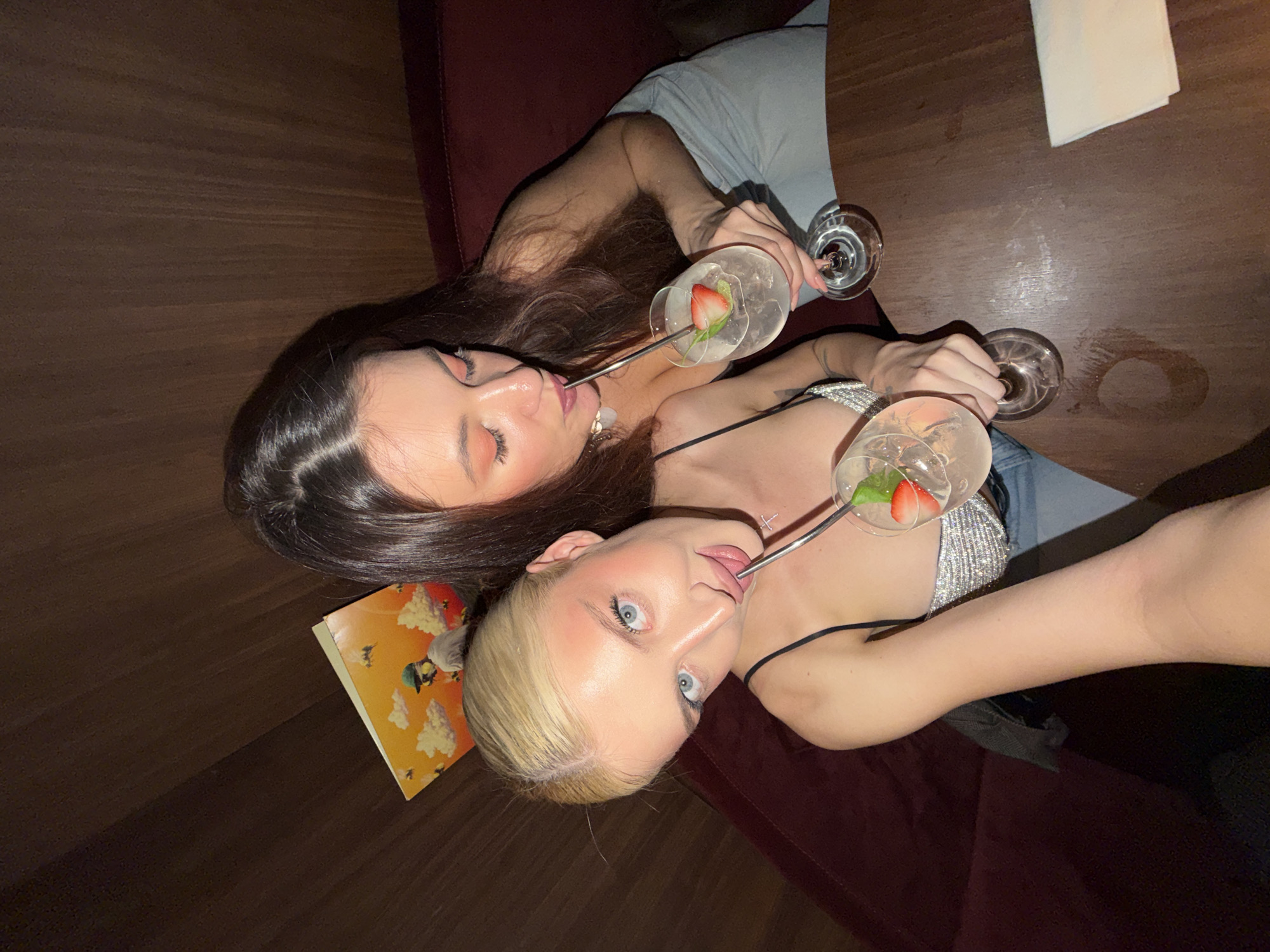 Two women share cocktails at wooden table