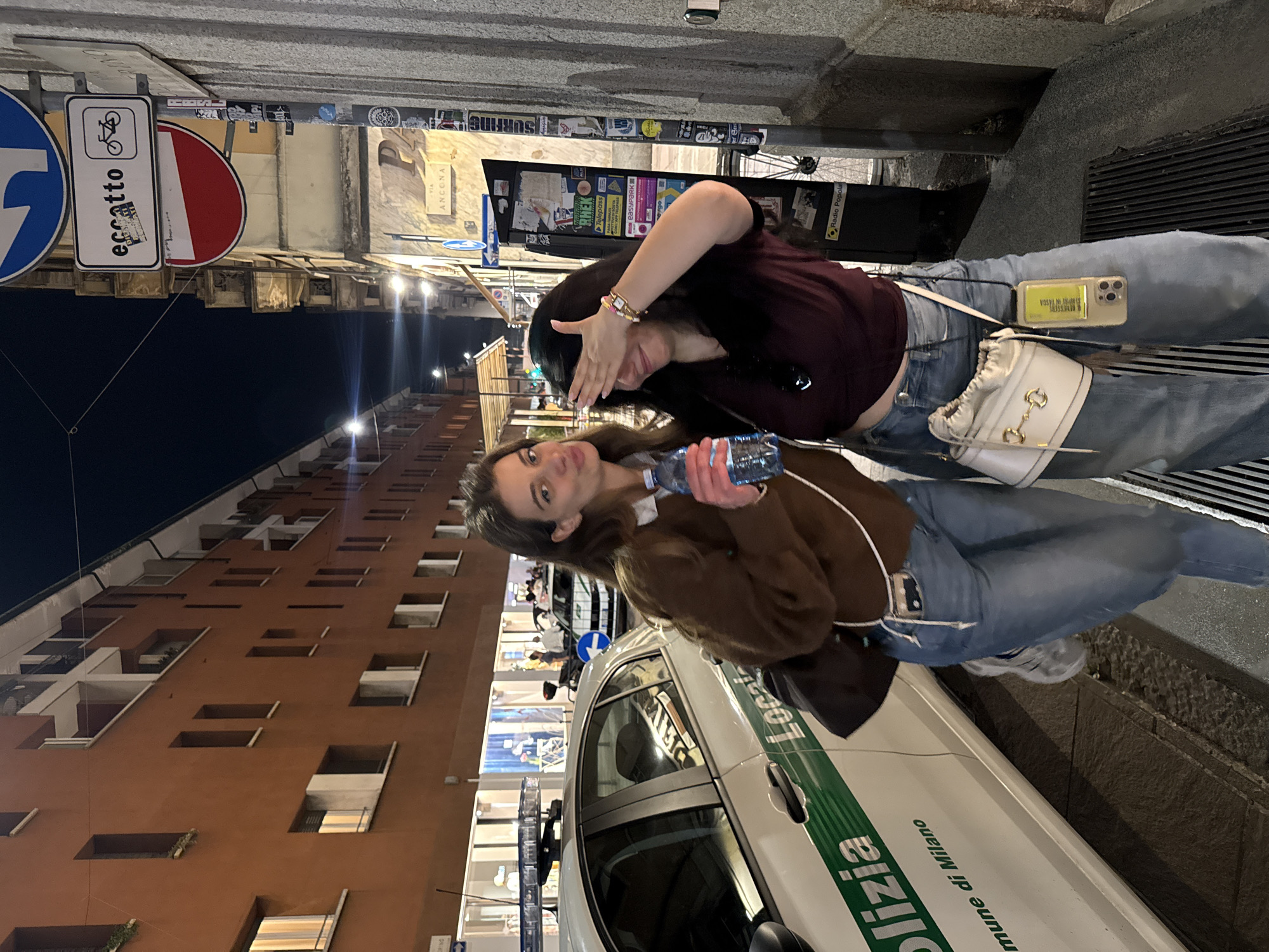Two women pose on Milan street near police vehicle