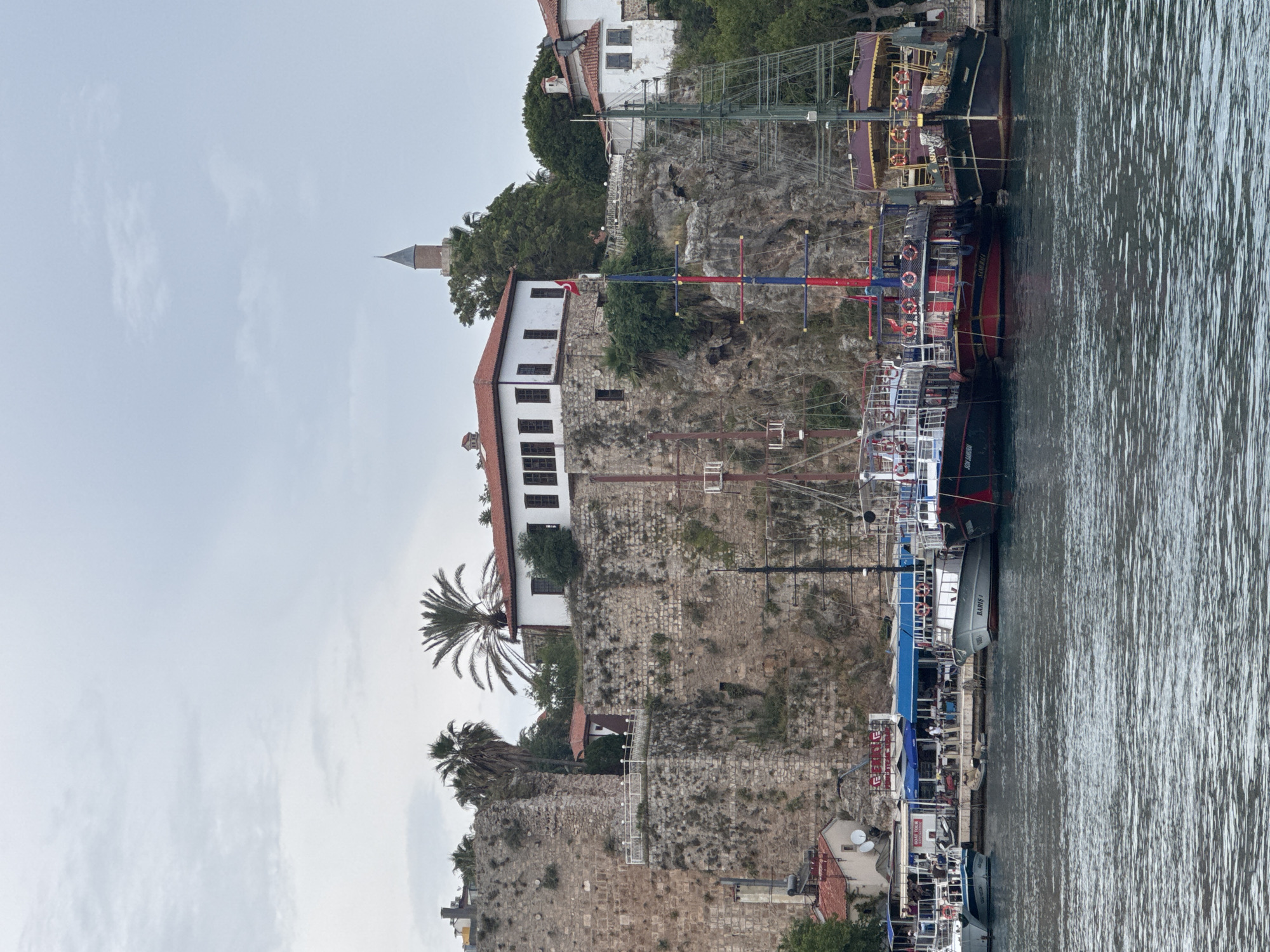 Tourist boat sails past historic Antalya clifftop fortifications