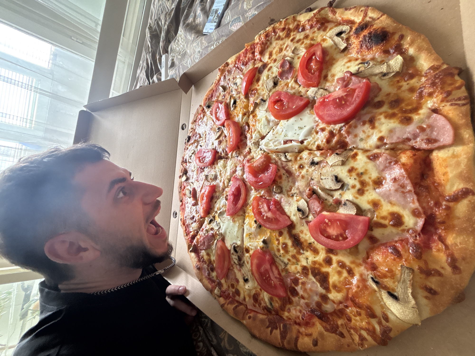 Man examines large topped pizza outdoors in black shirt