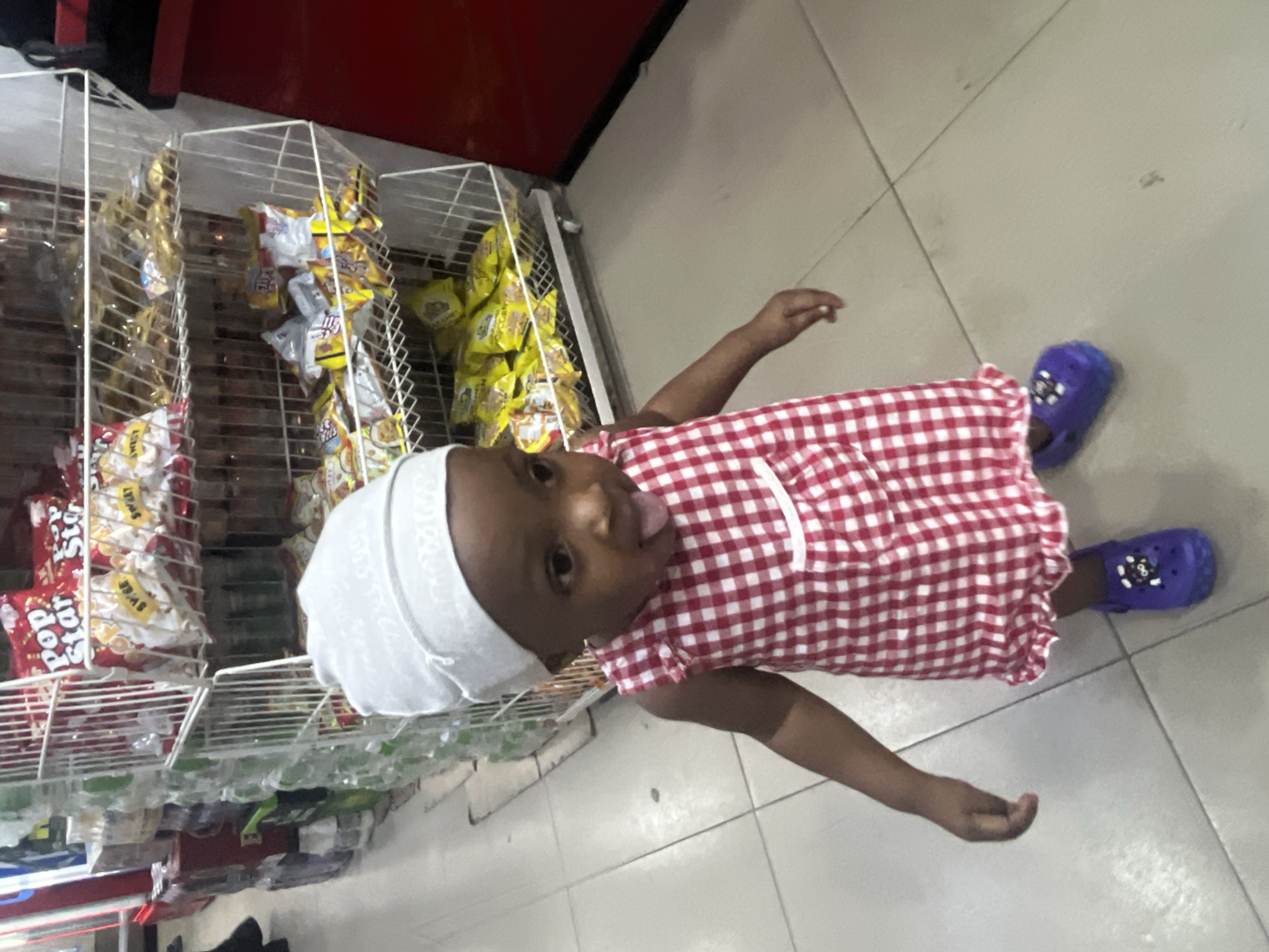 Toddler in checkered dress spotted playing in Nigerian grocery stores