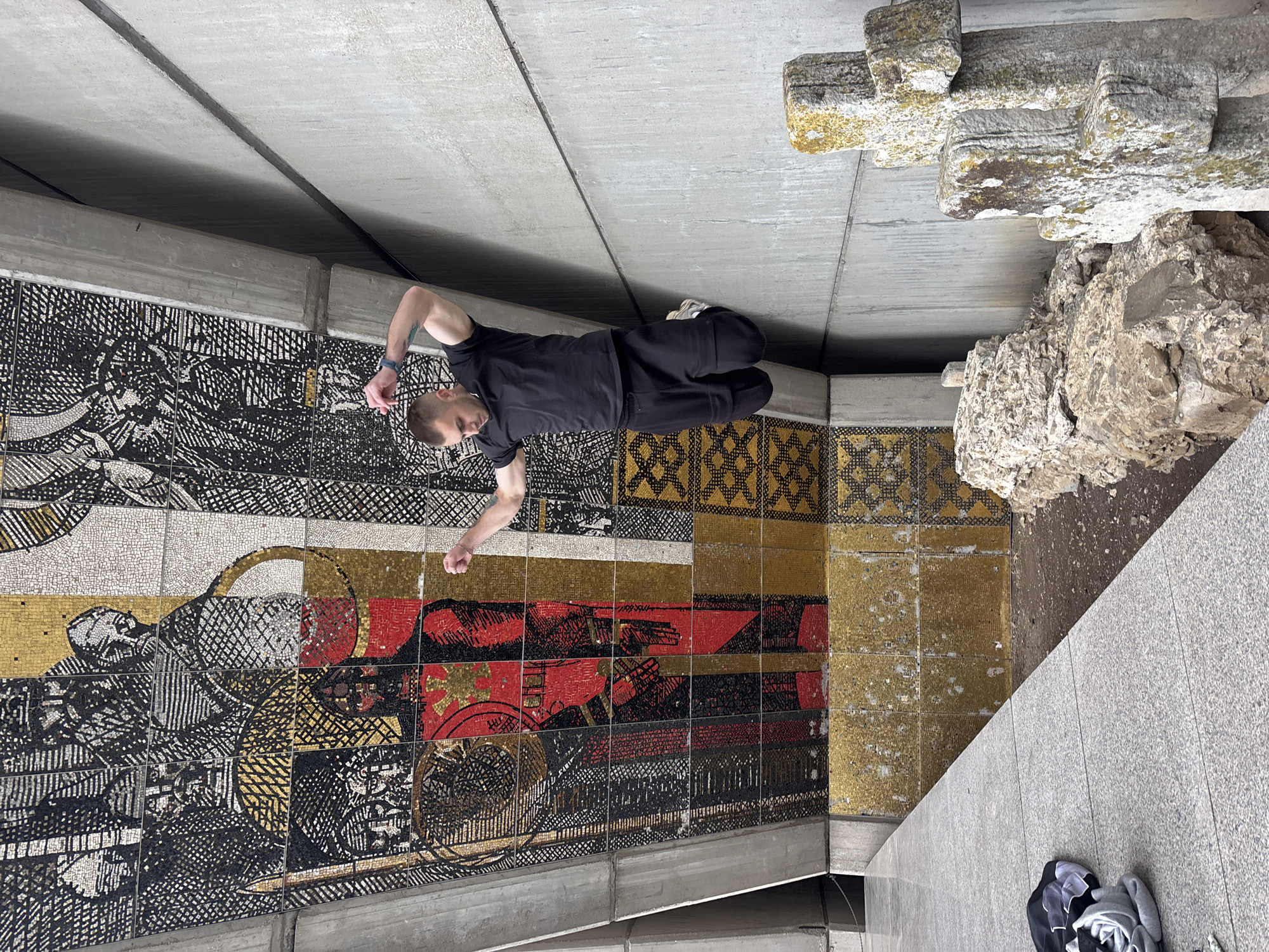 Man lies on concrete floor near large mosaic wall