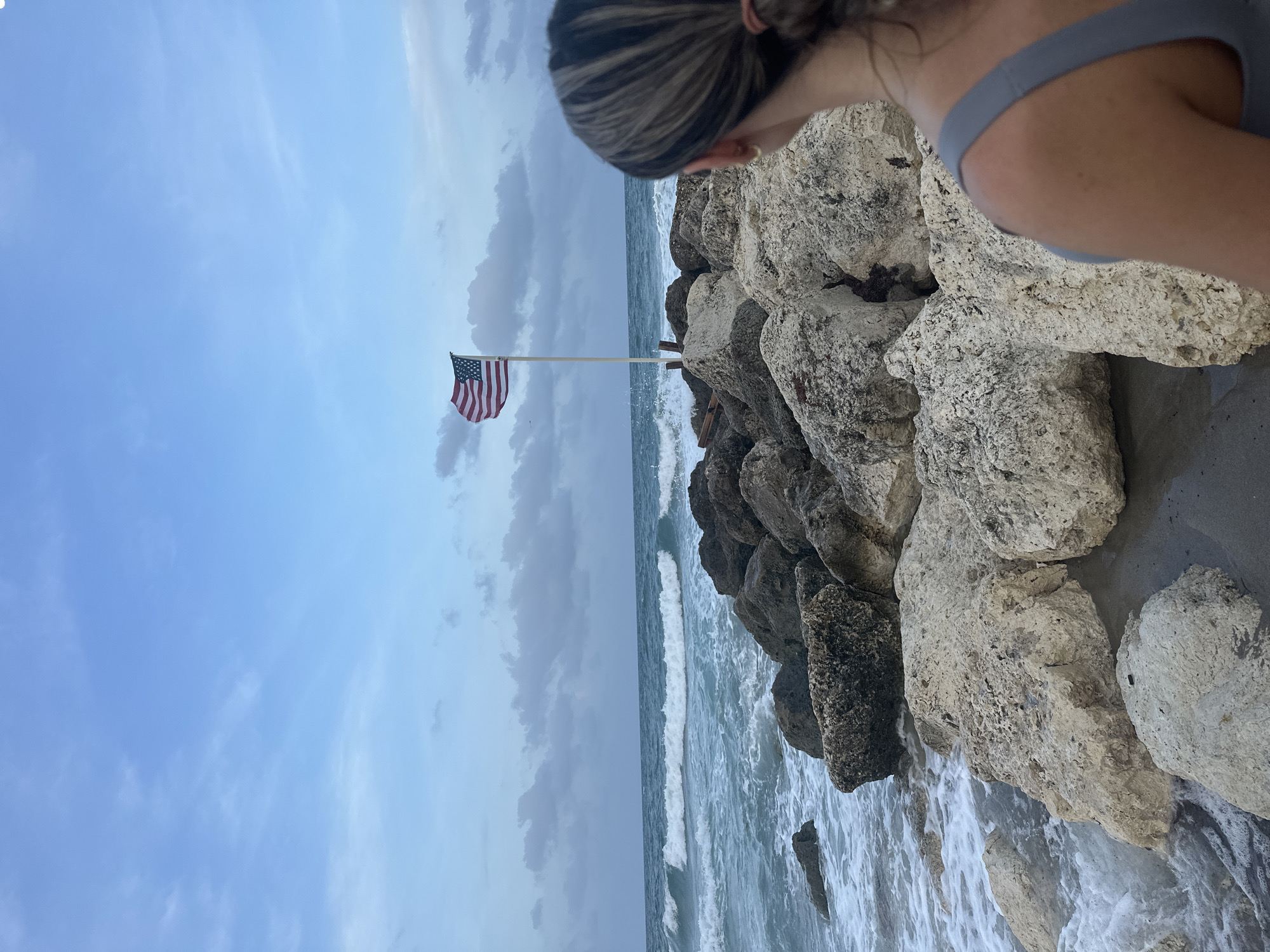 Woman watches ocean waves by flagged rocks in Boca Raton