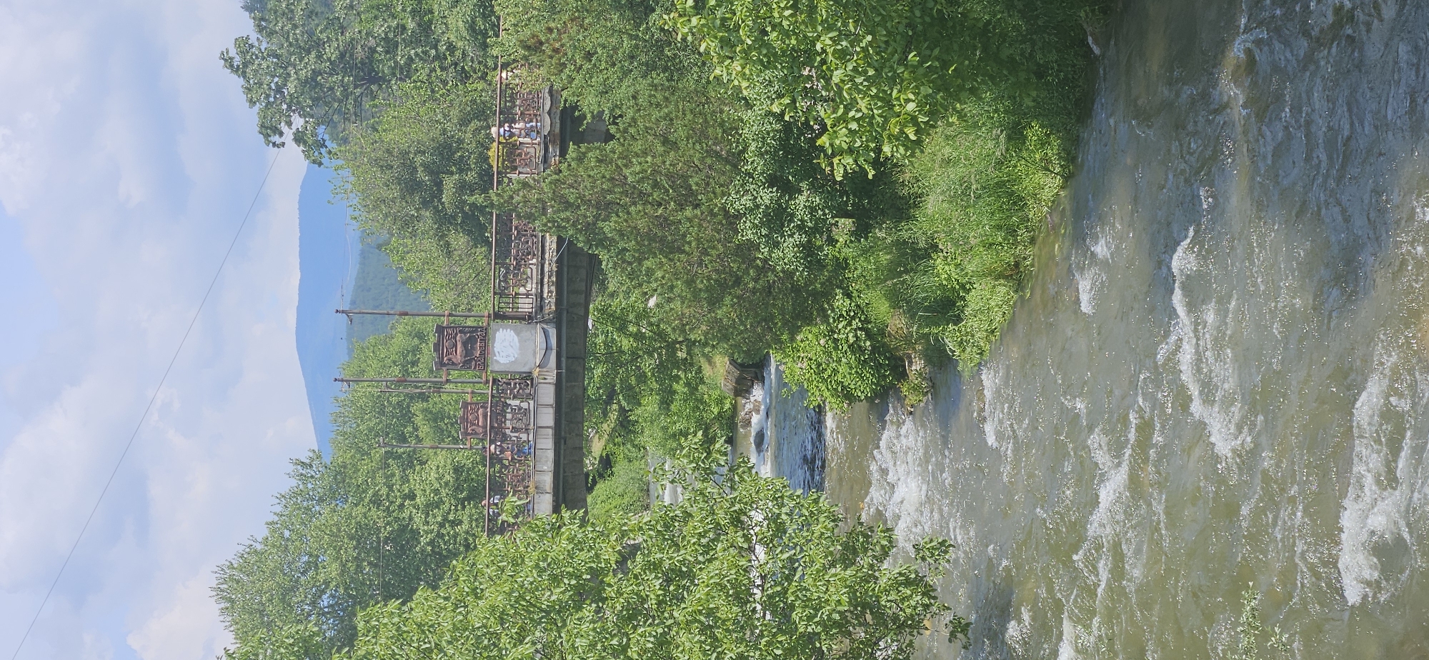 People cross old iron bridge over rushing river