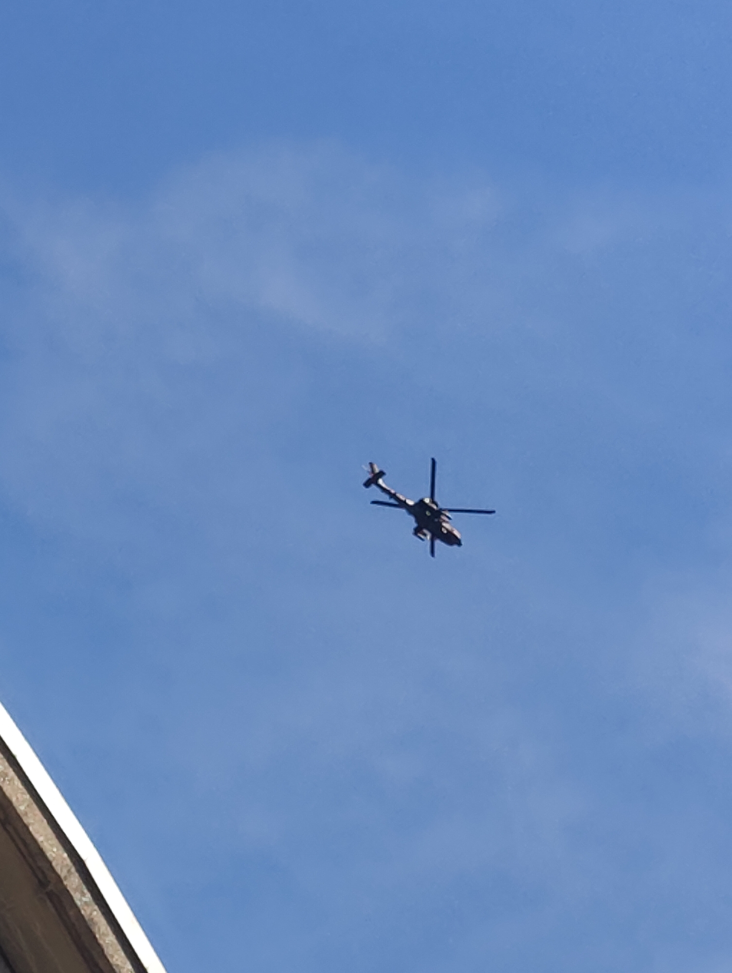 Dark helicopter climbs through a clear blue sky