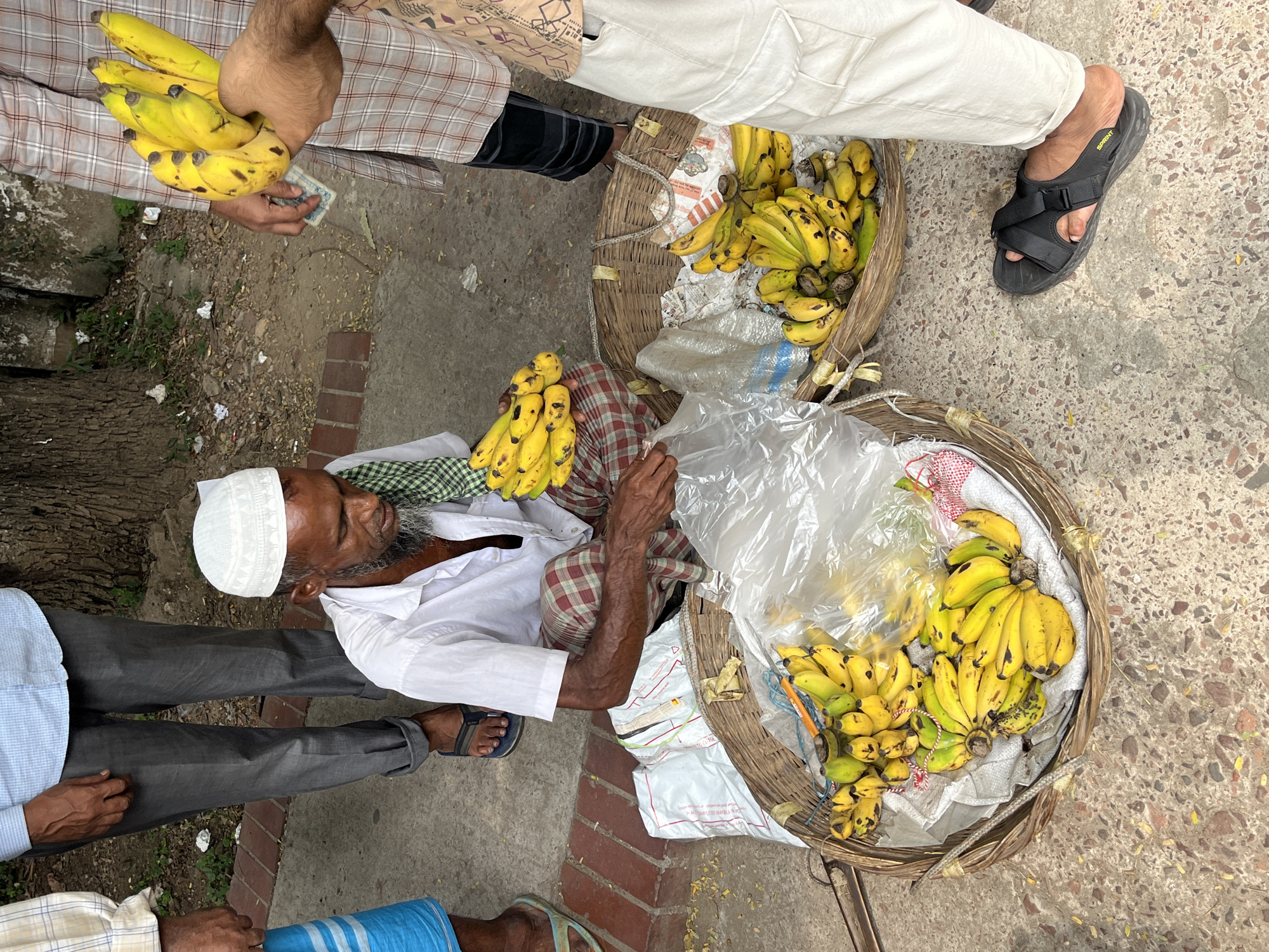 Elderly banana vendor sits at morning marketplace in Dhaka
