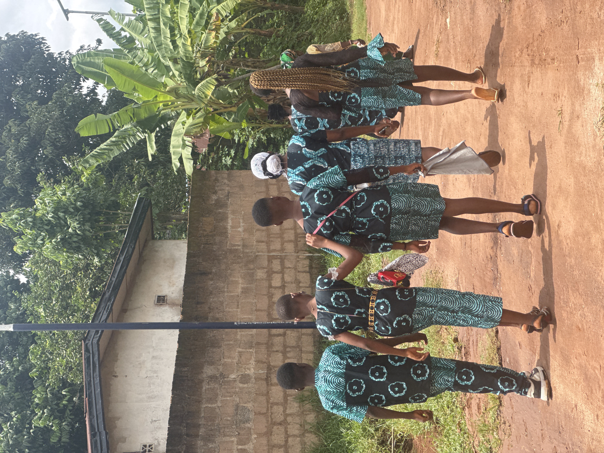 Five women in matching dresses walk through Eziudo, Nigeria
