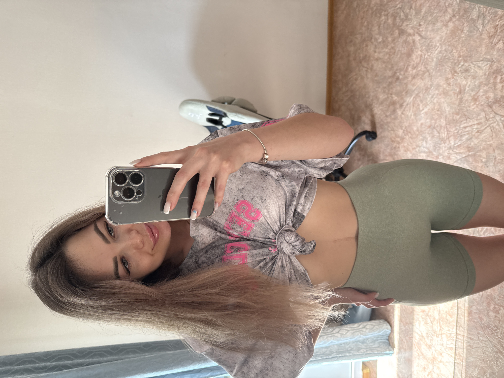 Woman takes selfie indoors wearing knotted shirt, green shorts