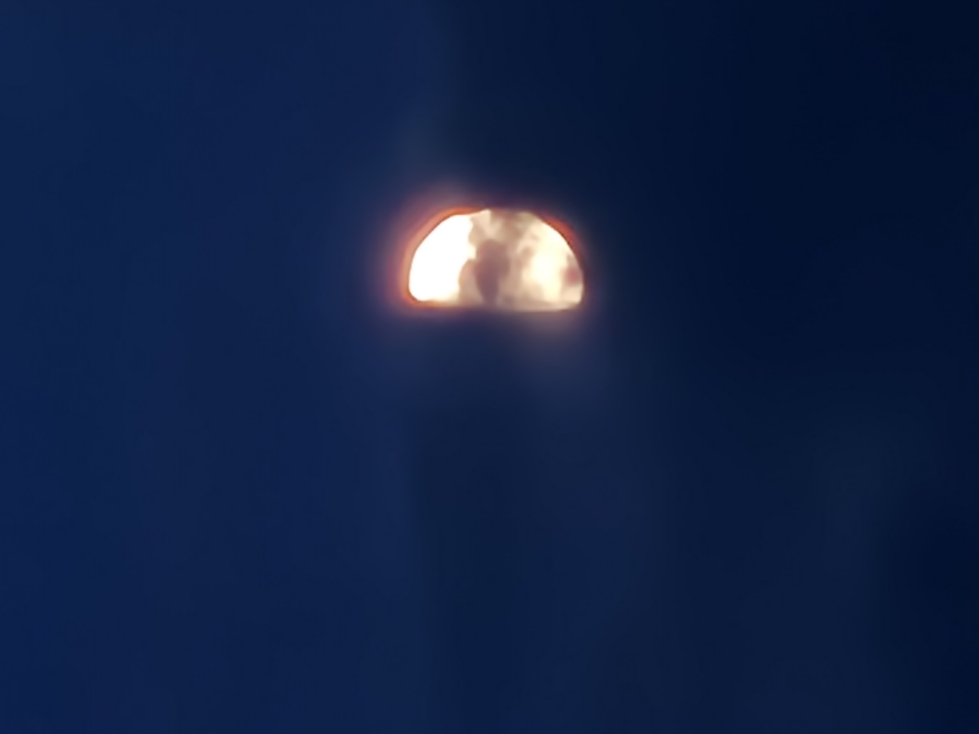 Waxing gibbous moon partly veiled by clouds in a dark sky