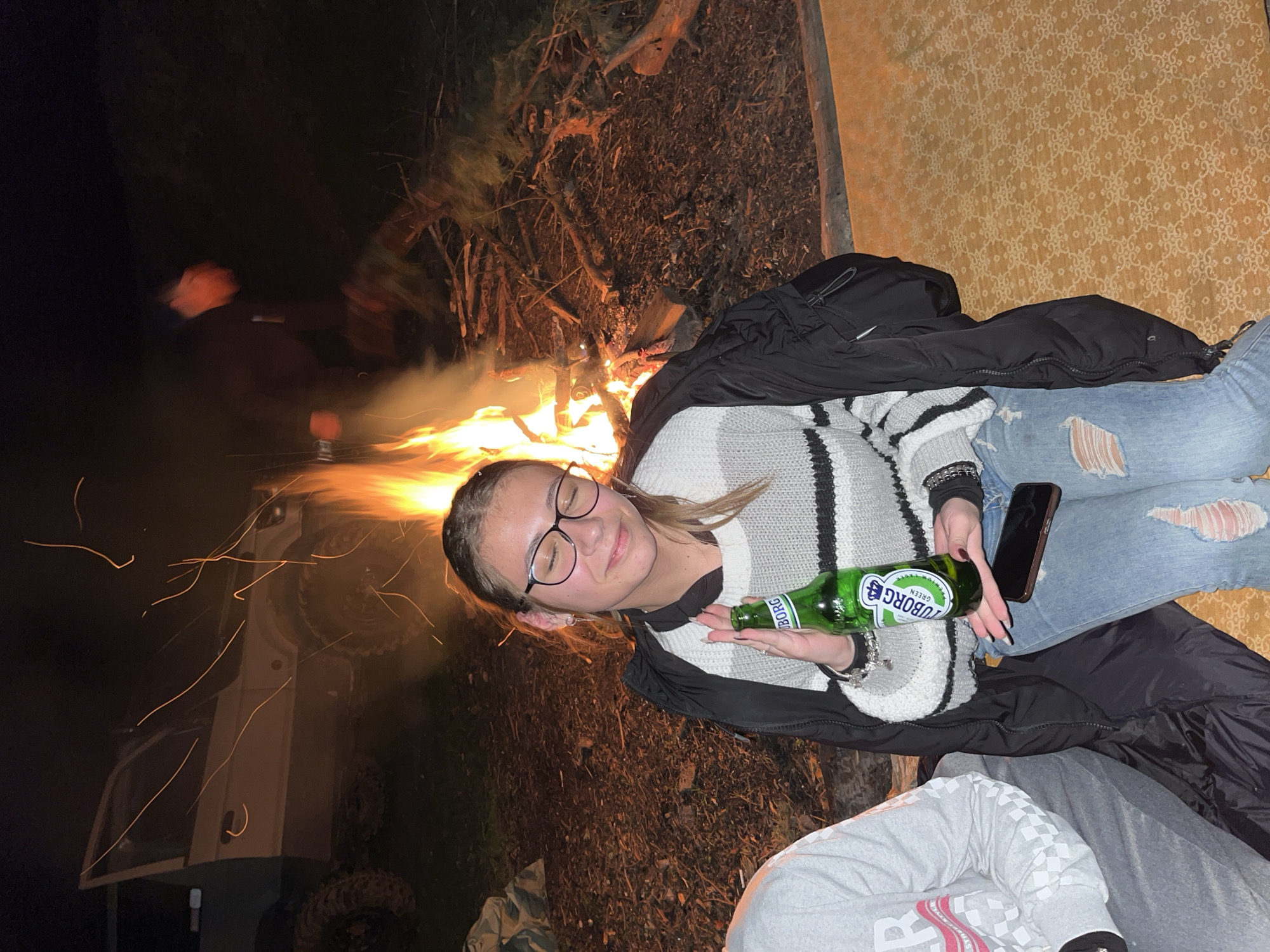 Woman enjoys evening campfire with beer in Karavelovo, Bulgaria