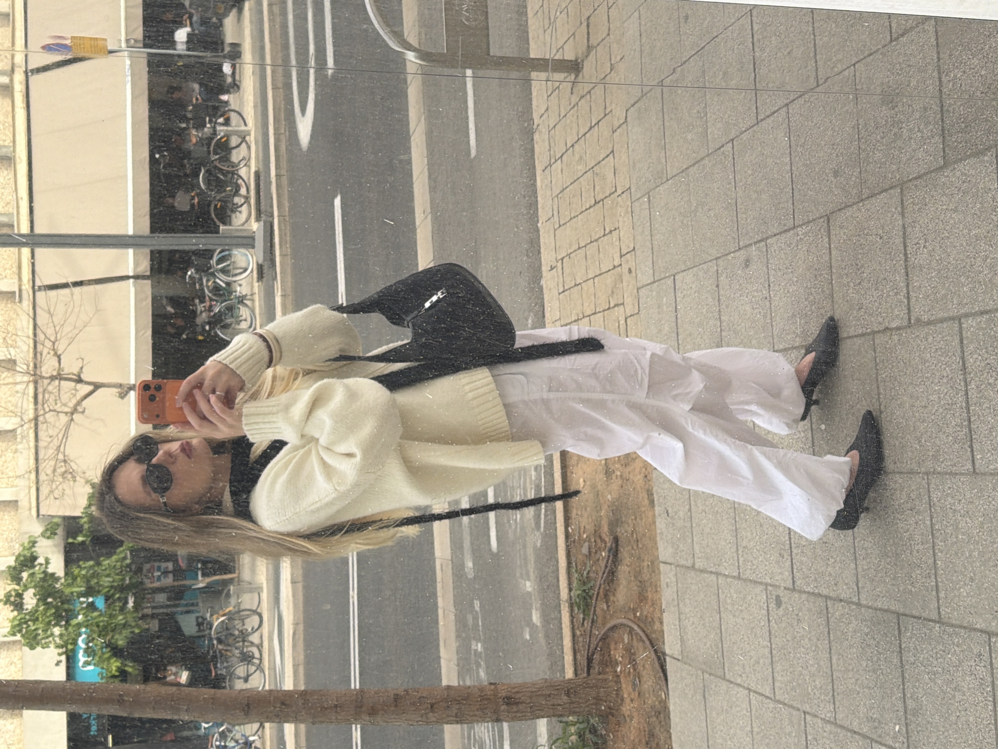 Woman reflected in Tel Aviv storefront window while using phone
