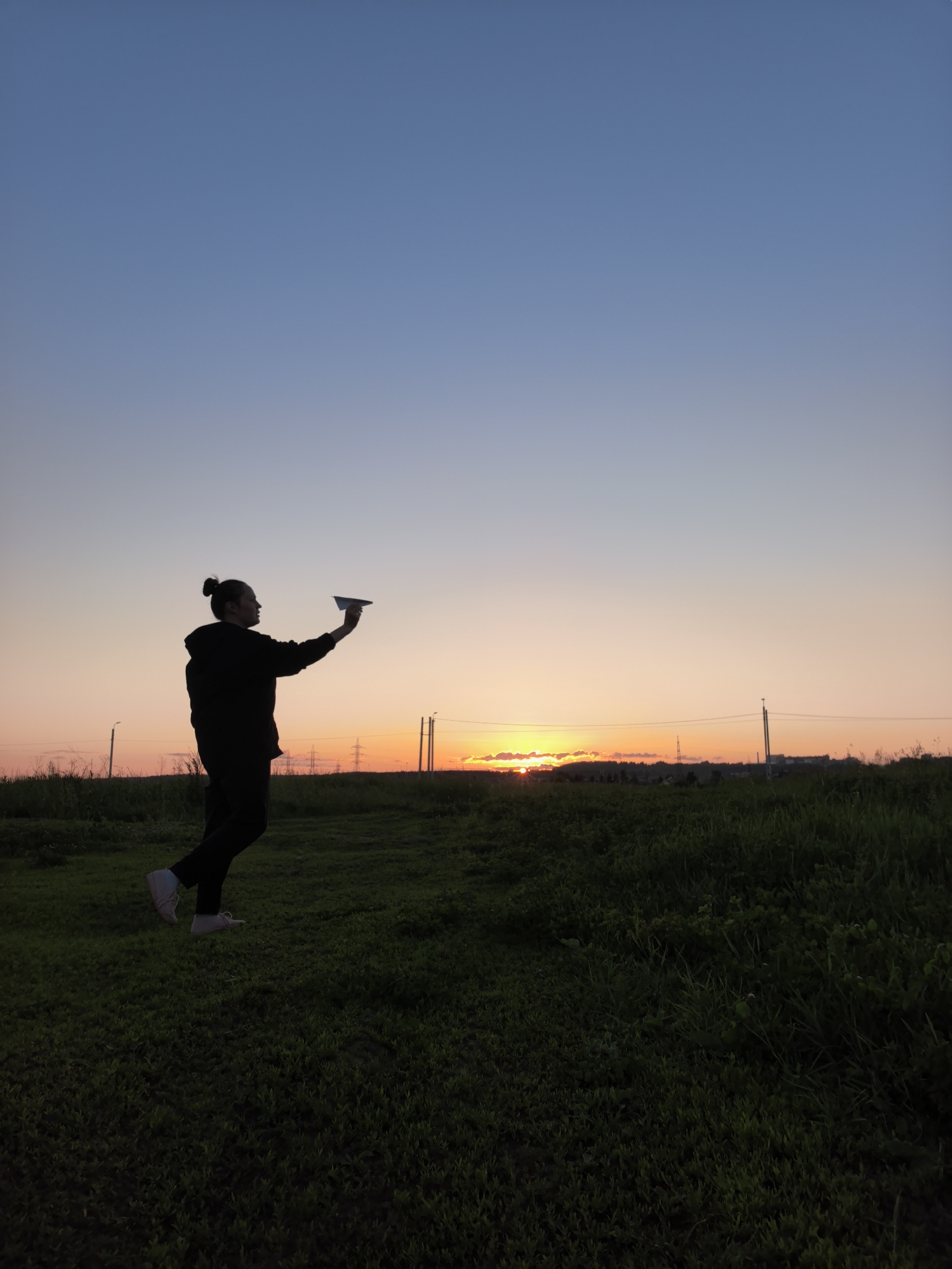 Person plays with paper airplane in field at sunset