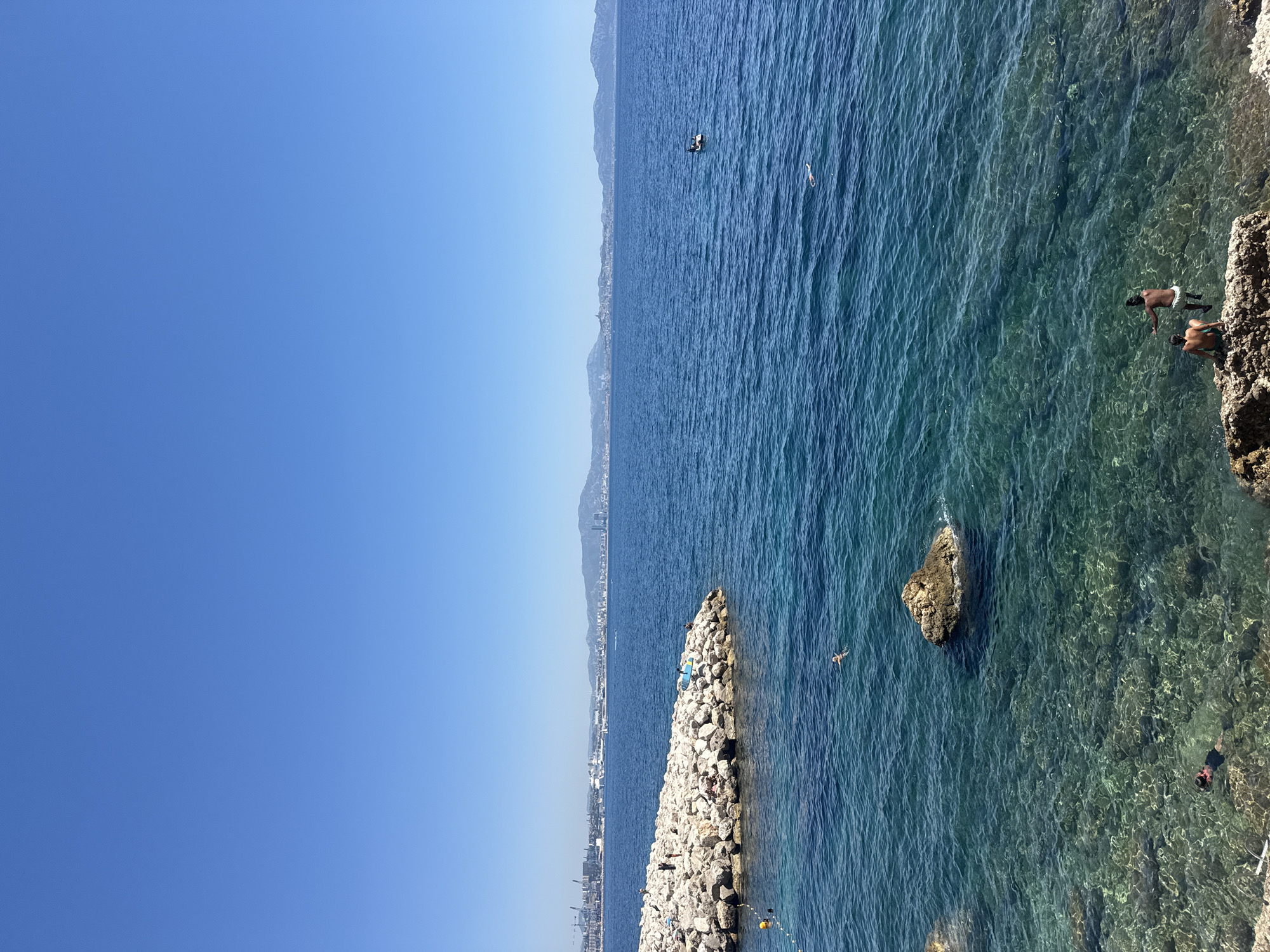 Sunny day along a rocky coastal path near a city.