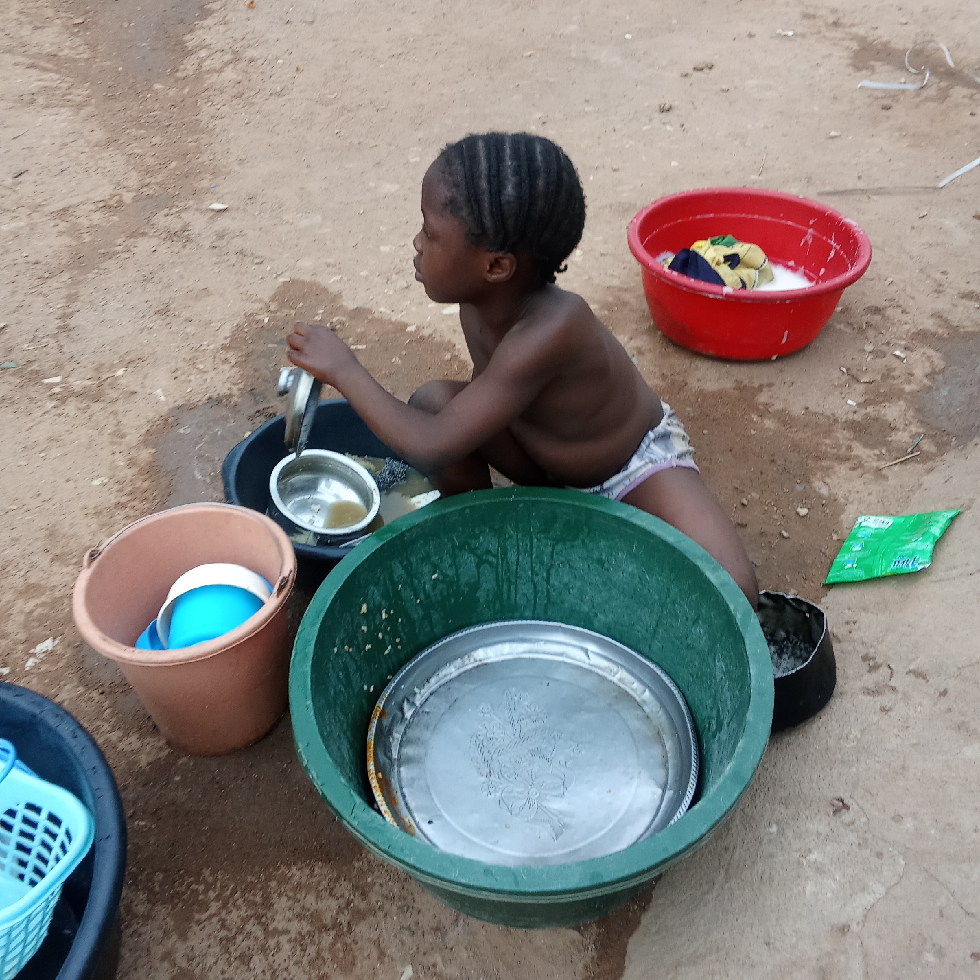 Child washing dishes outdoors in Akwanga, Nigeria