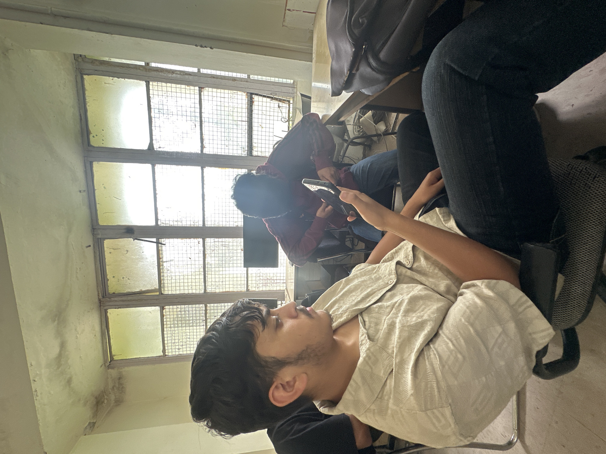 Friends killing time in a classroom, phones out, arm wrestling.