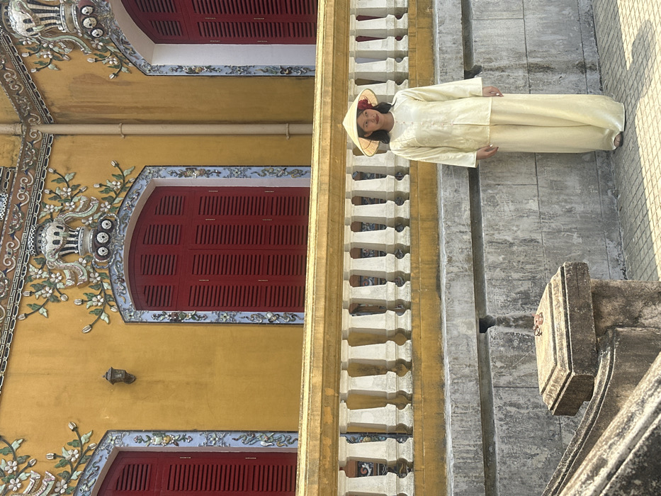 Woman stands before yellow structure in Hue Imperial City