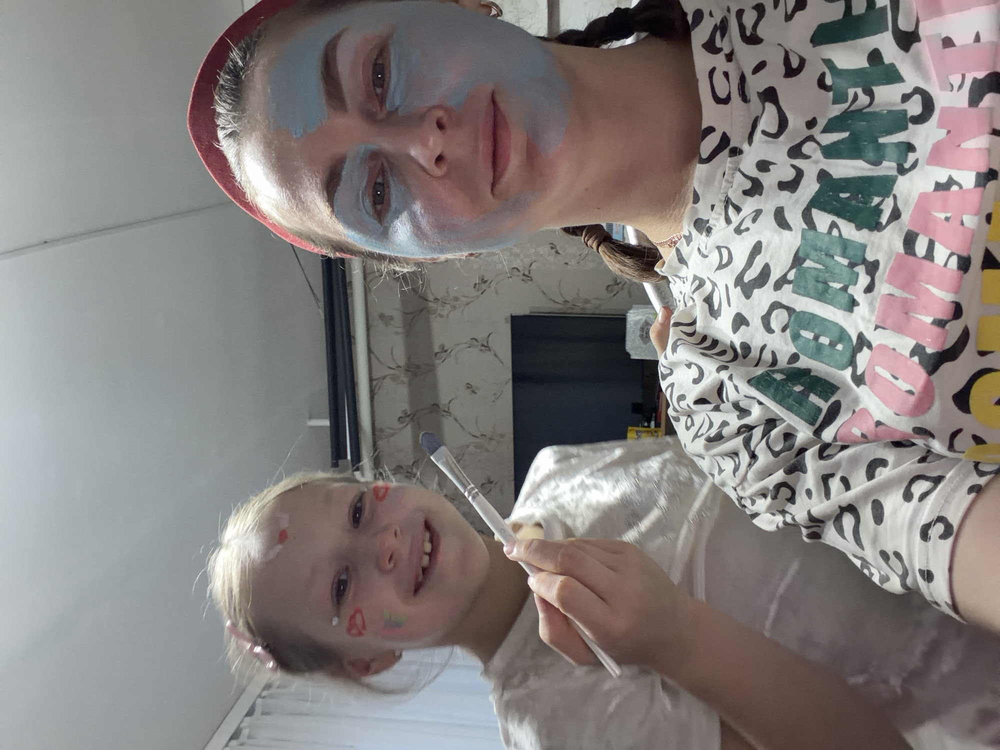 Child applies blue face paint to woman in Russian home