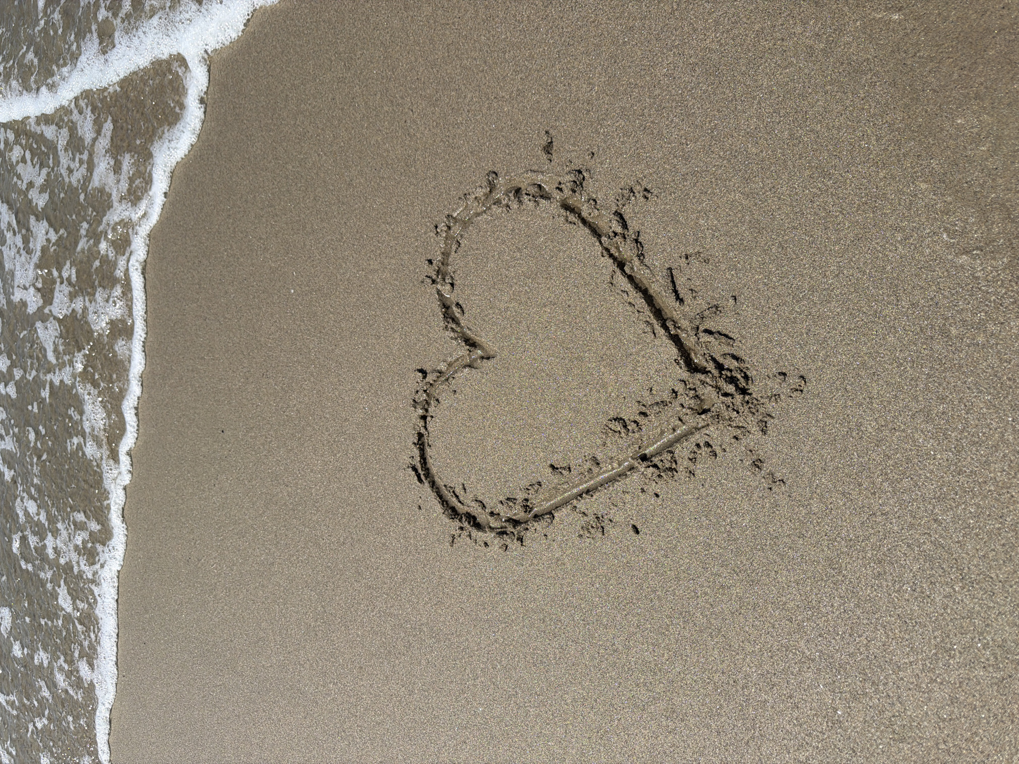 Sunny beach day: waves, a fading sand heart, and a quiet shoreline.