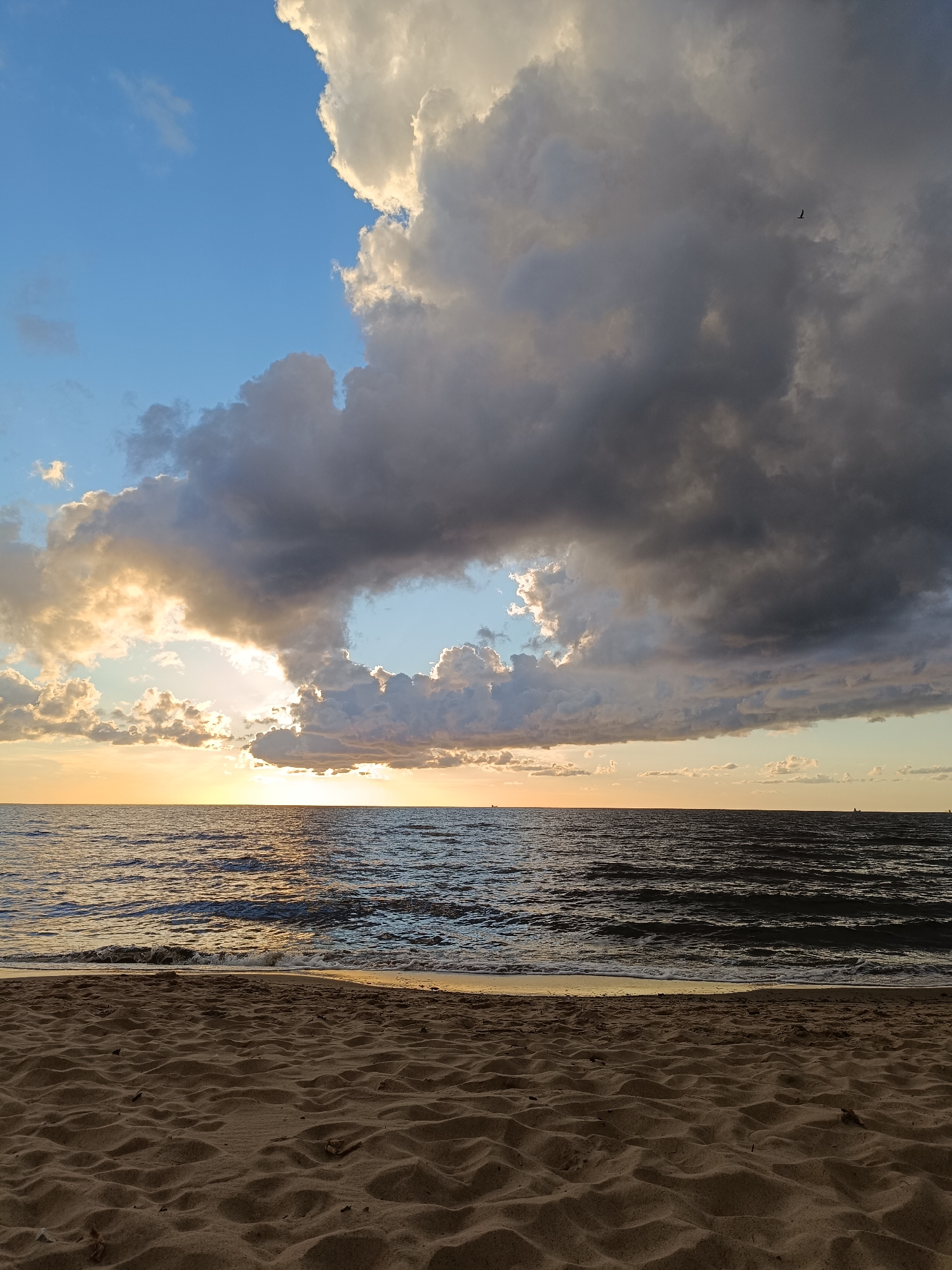 Beach at dusk: waves, a shelter, and a ship on the horizon
