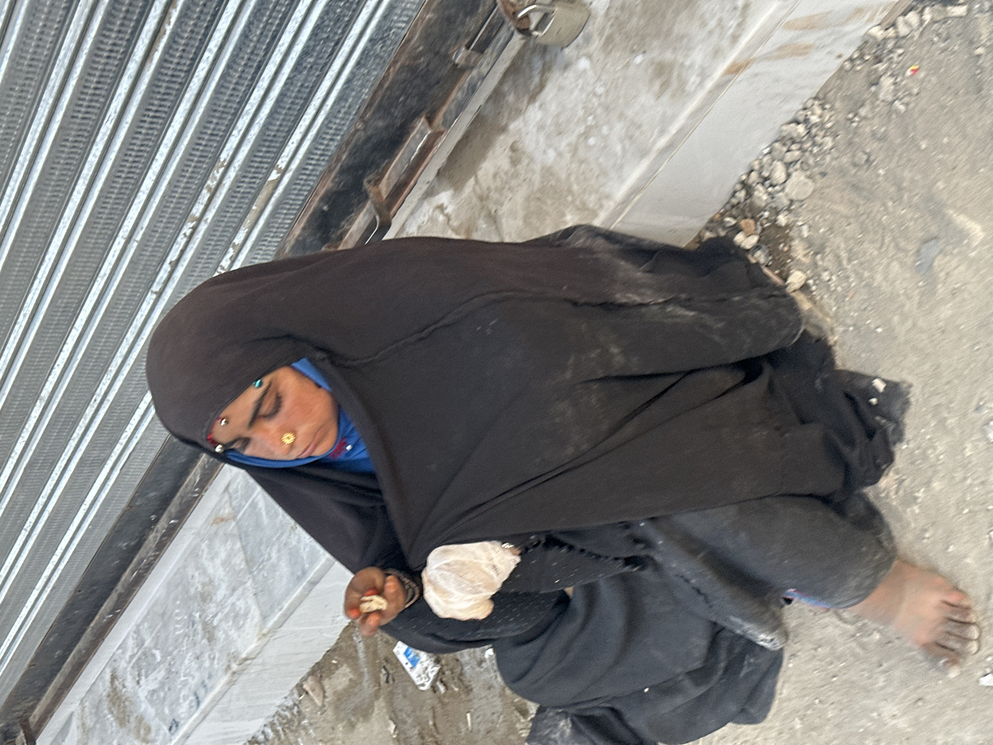 Elderly woman sits on Quetta sidewalk near closed shop