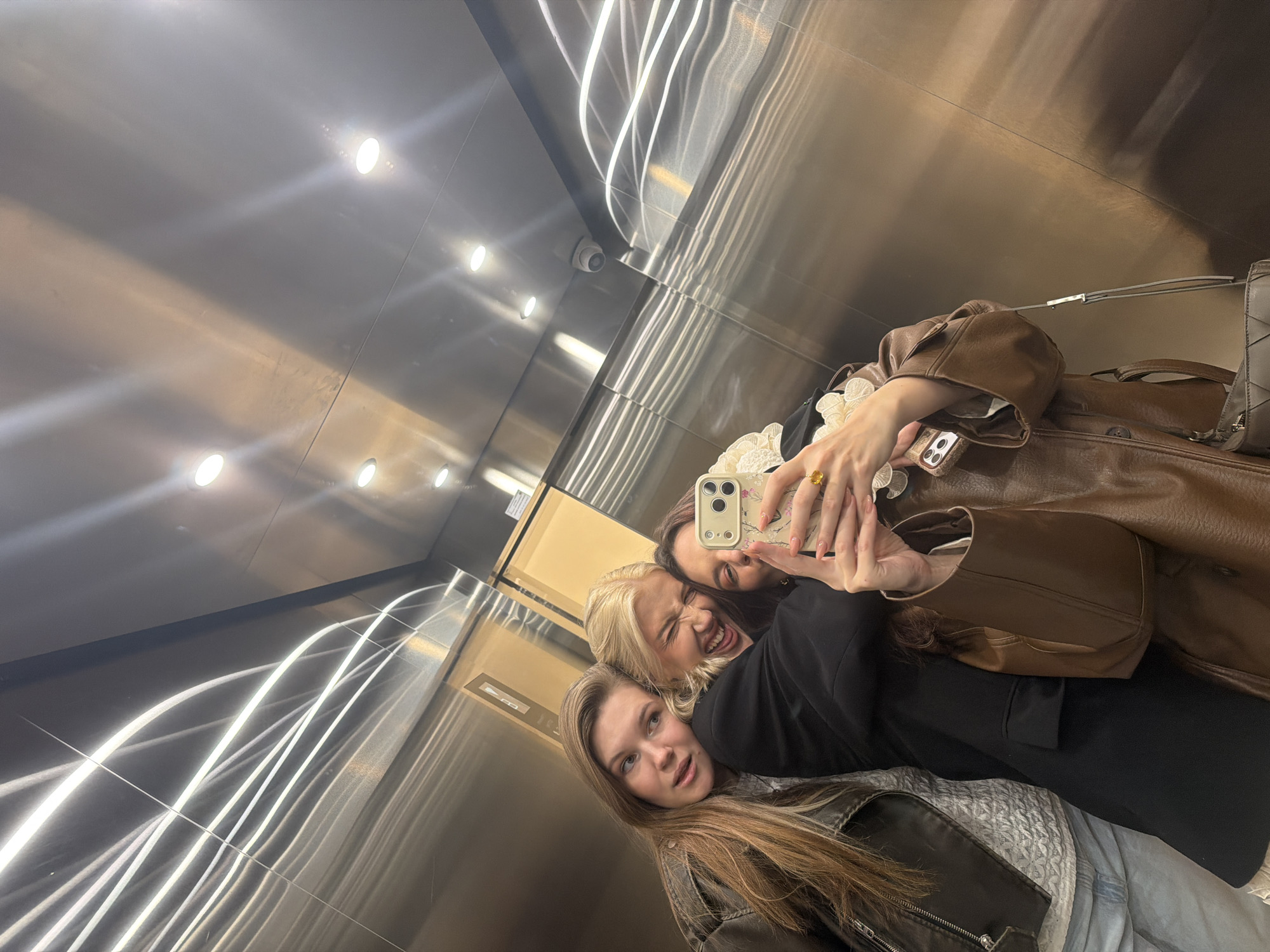 Three women take selfie in stainless steel elevator