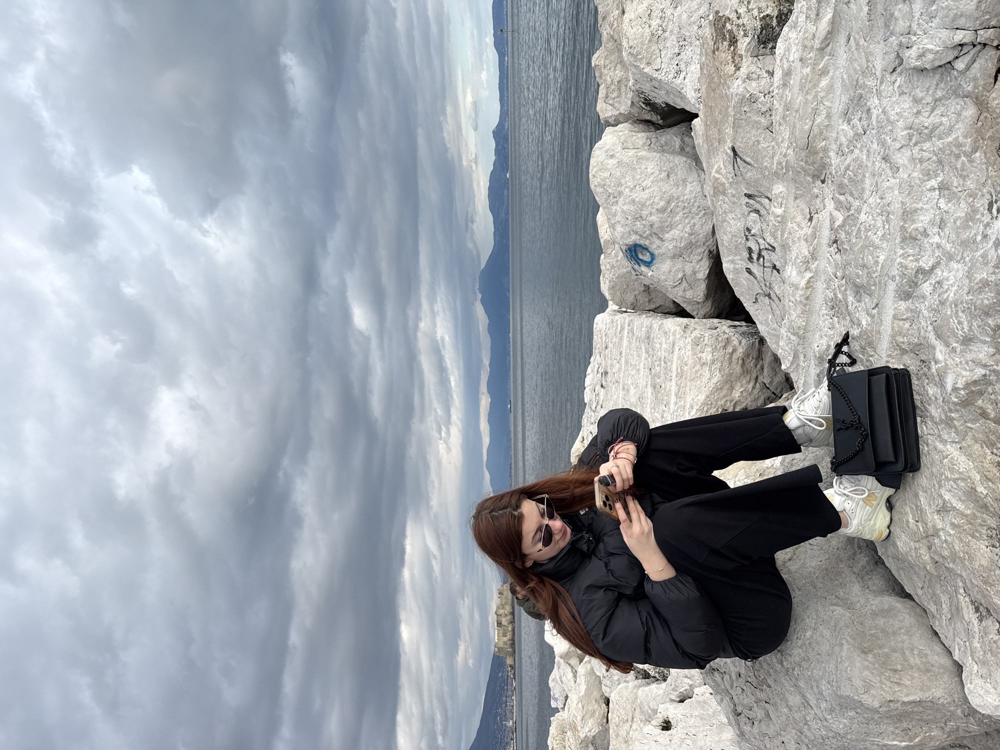 Woman sits on Naples breakwater under overcast skies