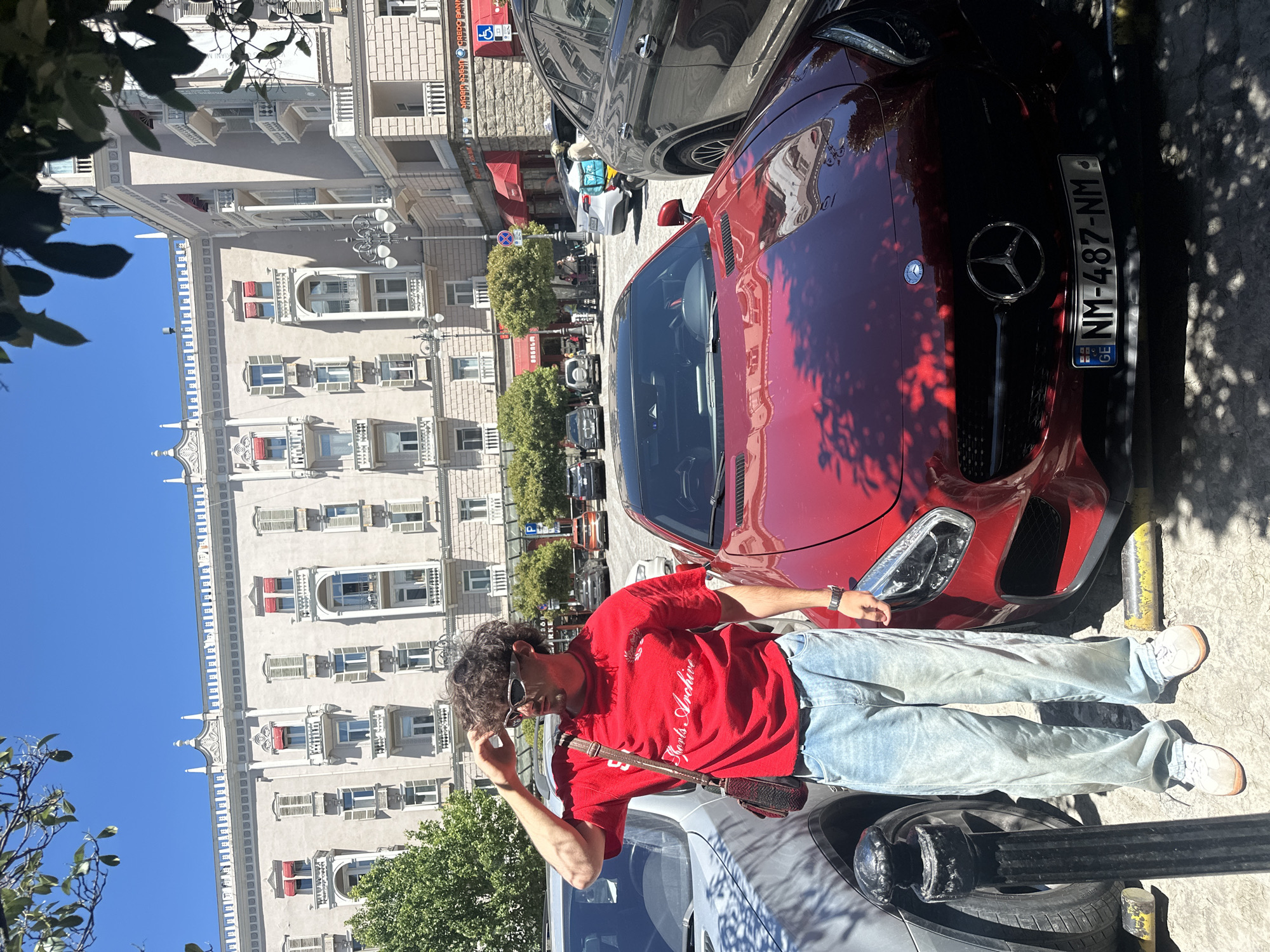 Young man poses with red Mercedes sports car around Tbilisi