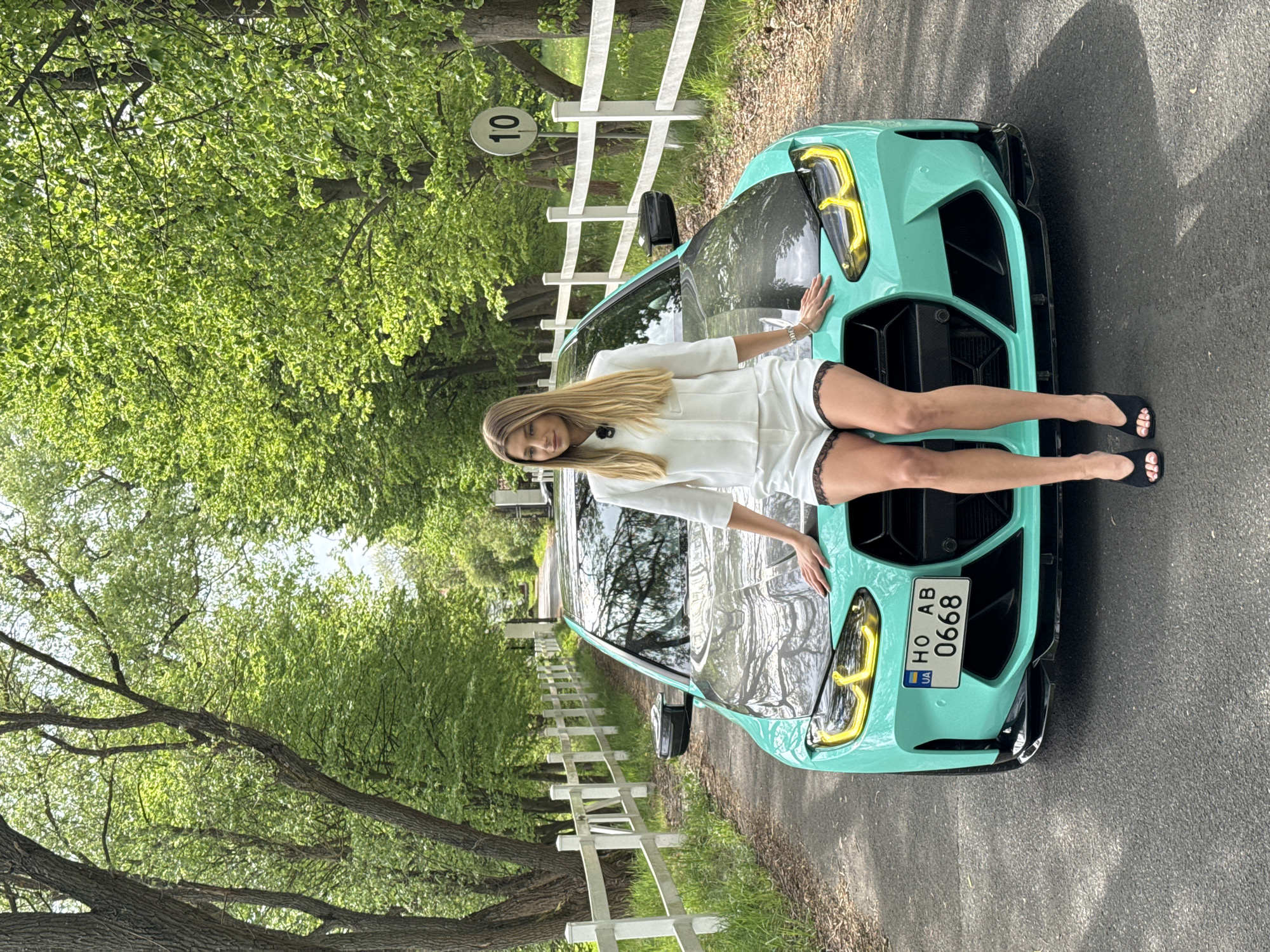Woman poses with turquoise BMW on tree-lined road