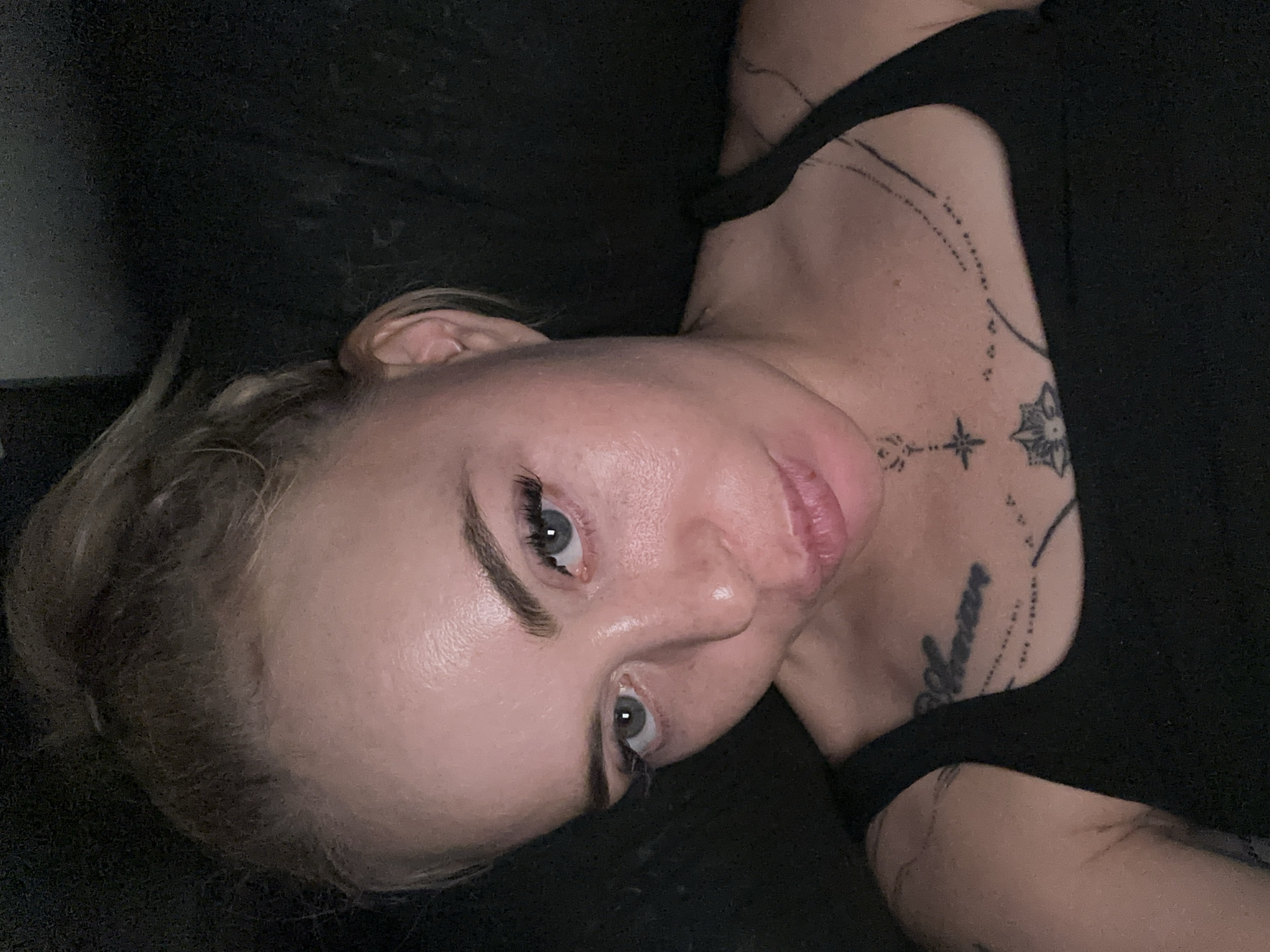 Tattooed blonde woman captures multiple selfies in dimly lit setting