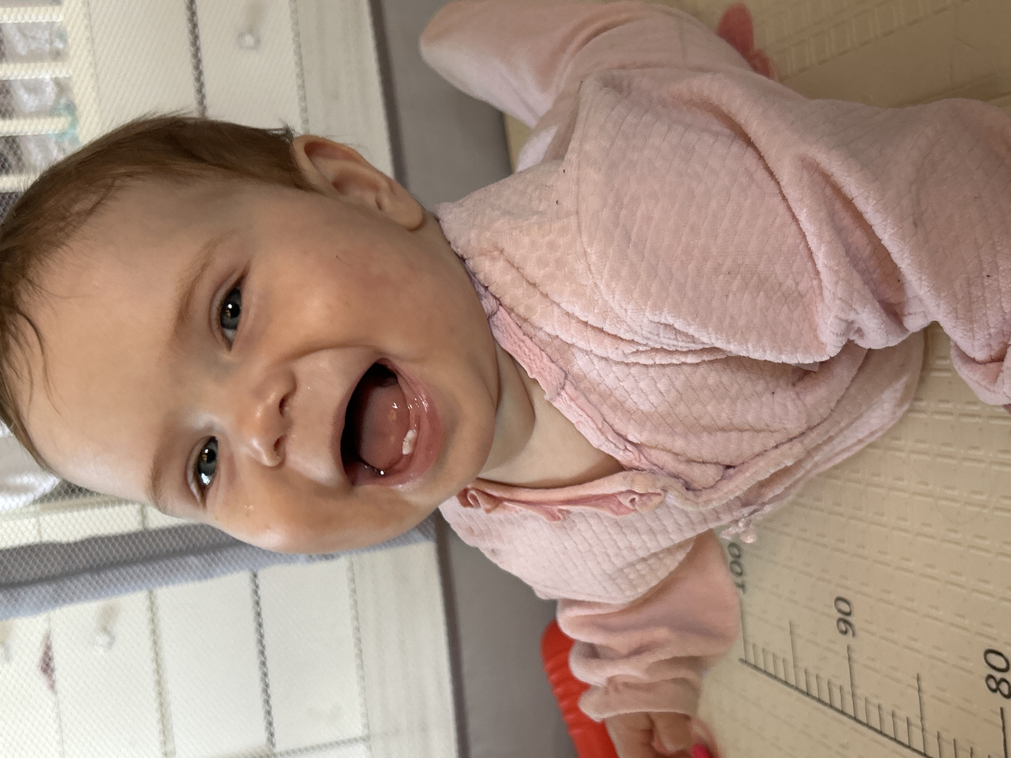 Baby in pink outfit smiles on mat in Rusalevka