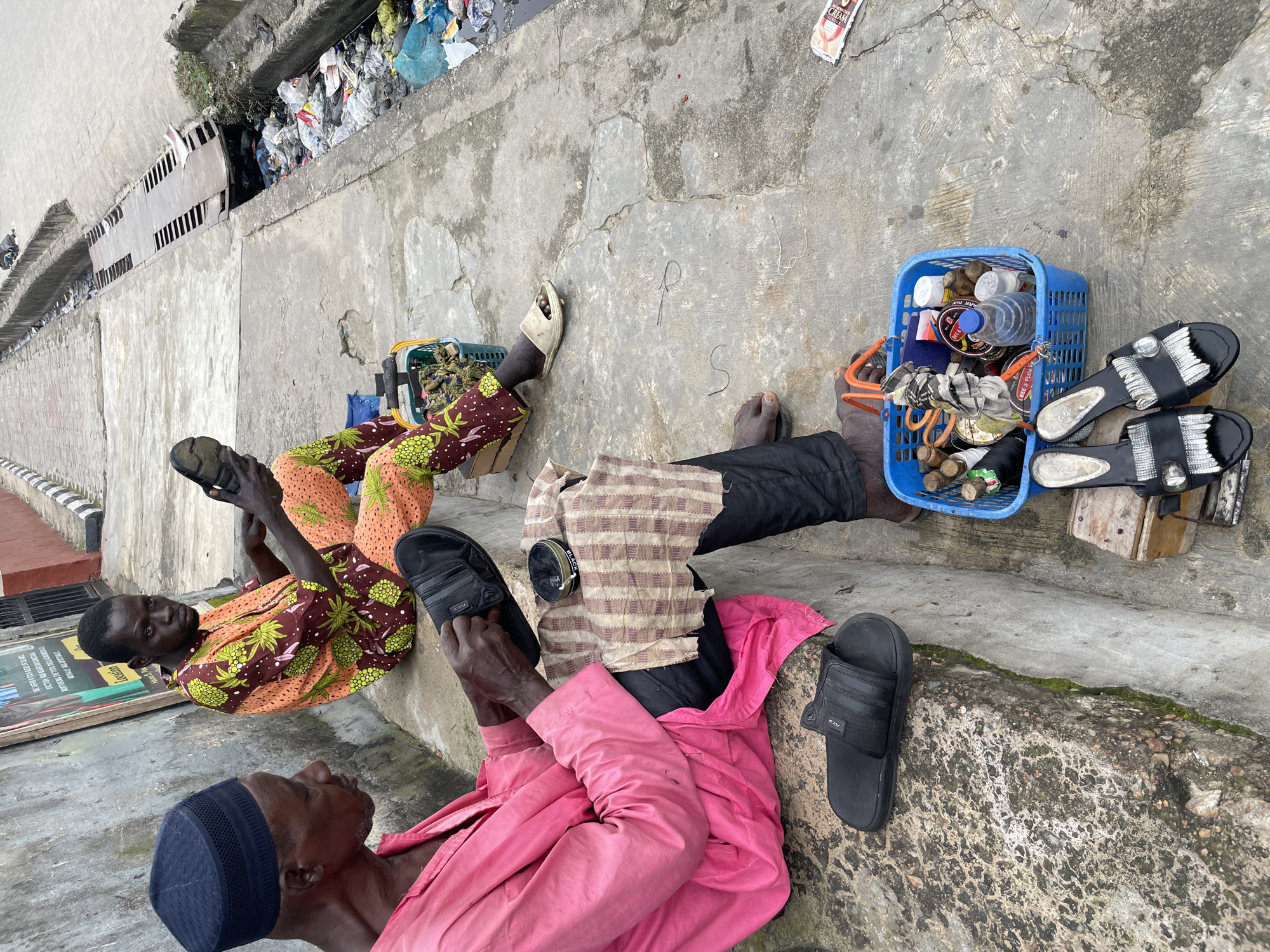 Cobblers at work on an Ado street, auto-rickshaw nearby