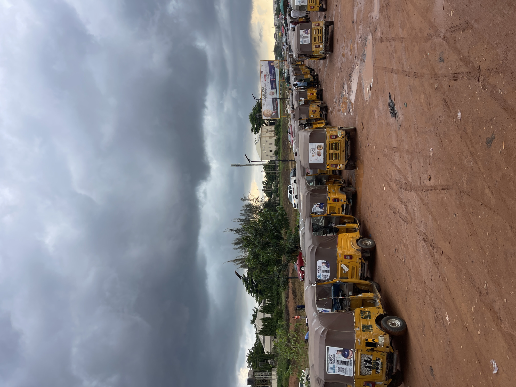 Keke Marwa queue up near a crowded overpass in rainy Galadimawa